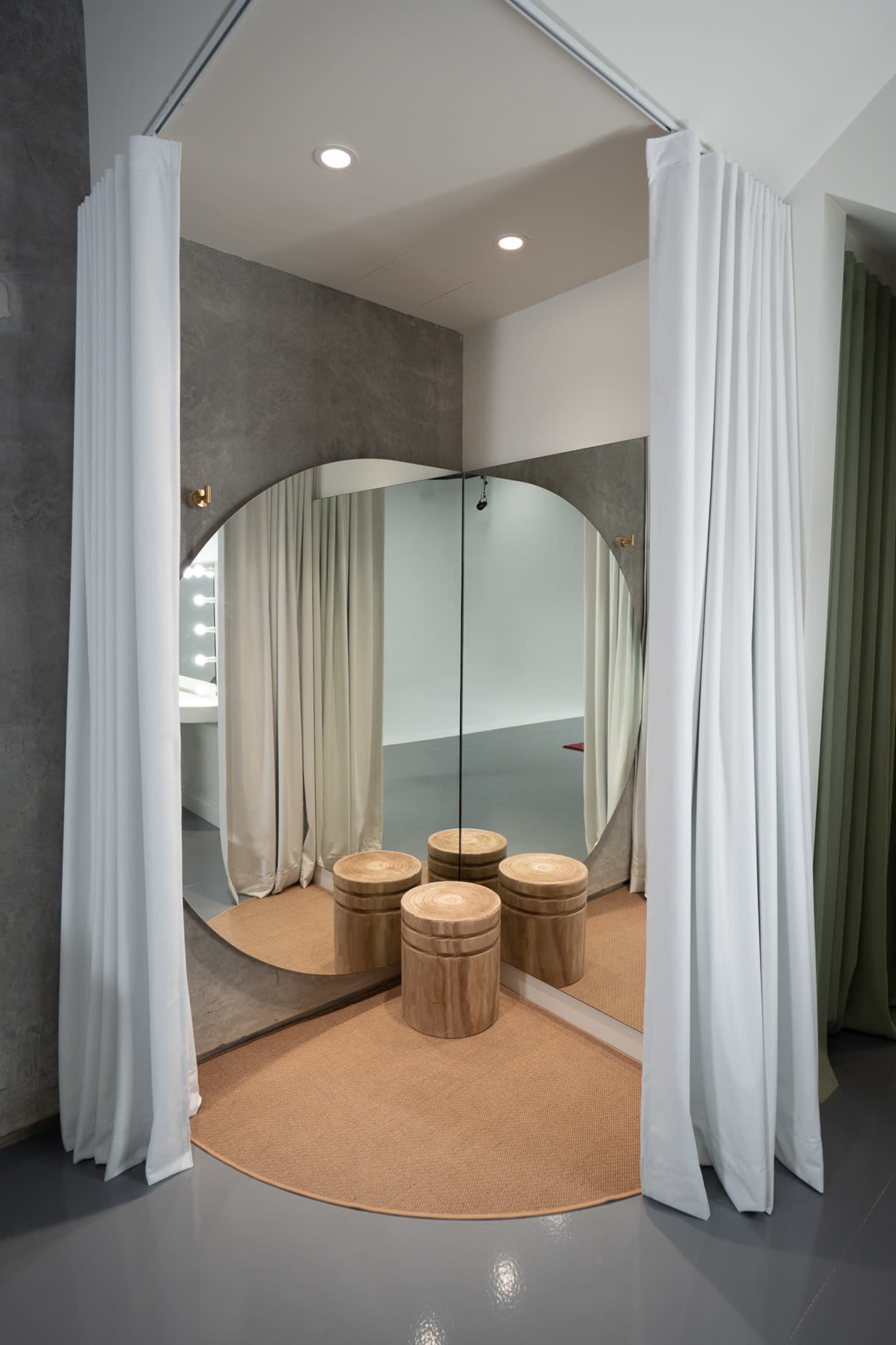 The image shows a circular mirror framed by curtains, with four wooden stools placed on a round mat in front of it.