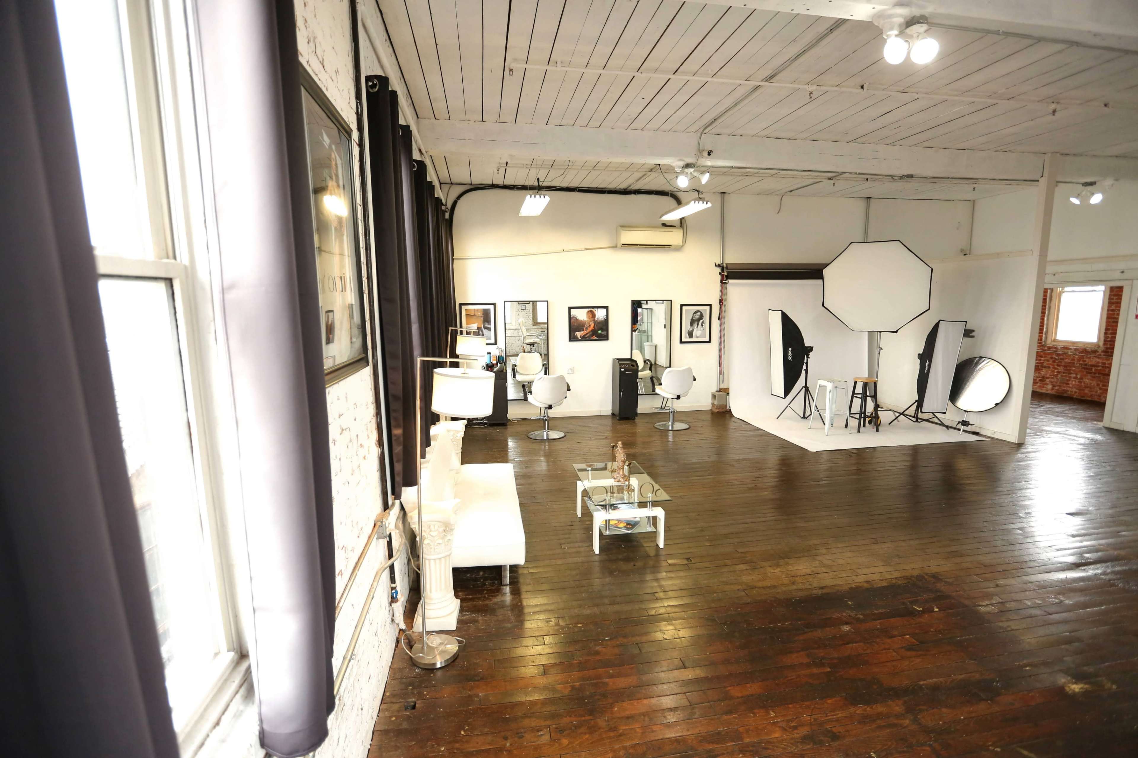 A spacious photography studio with a wood floor, white backdrops, lighting equipment, and framed photographs on the walls.