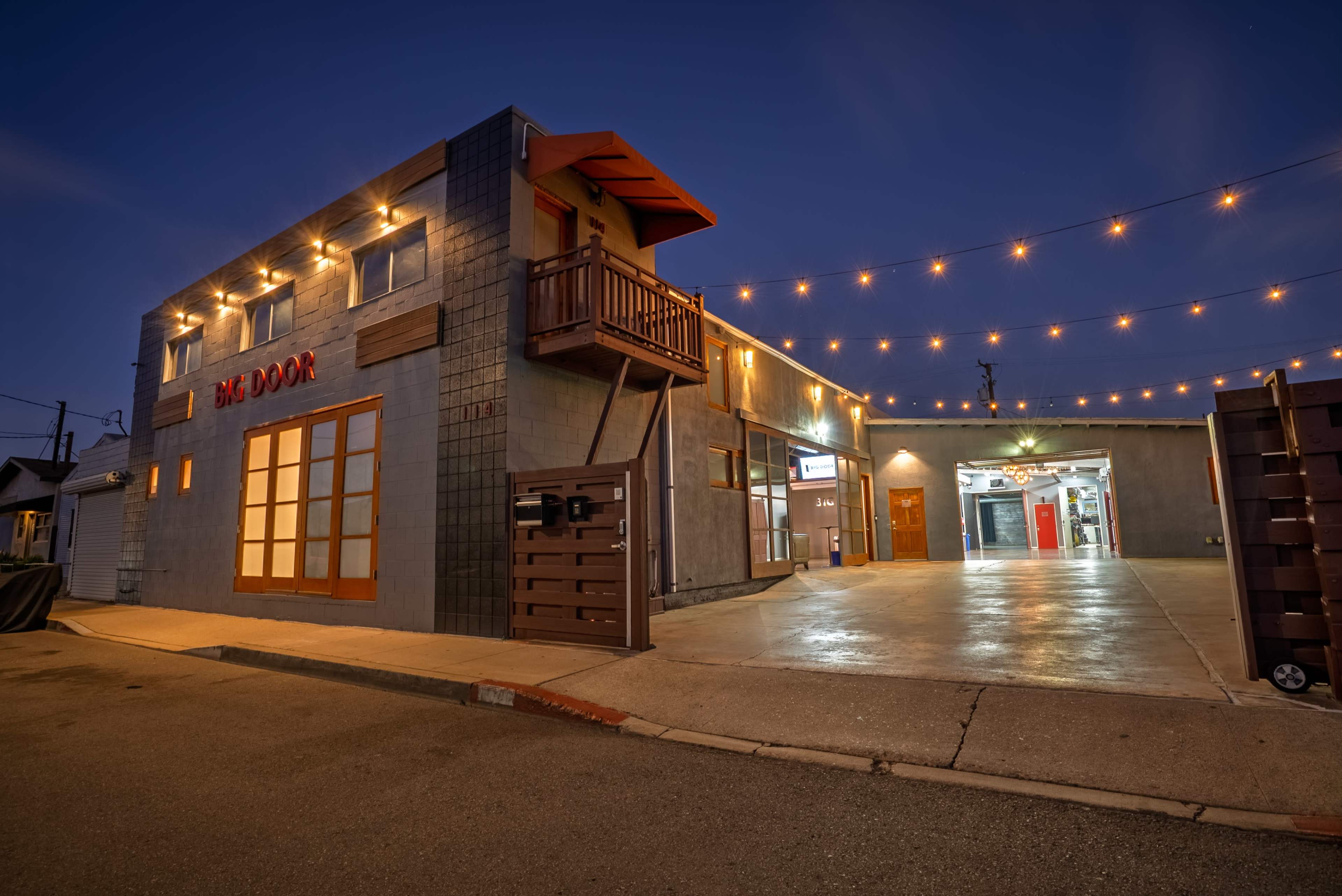 The image shows a modern building with a grey exterior, illuminated by string lights, and featuring the words "BIG DOOR" prominently displayed on the wall.