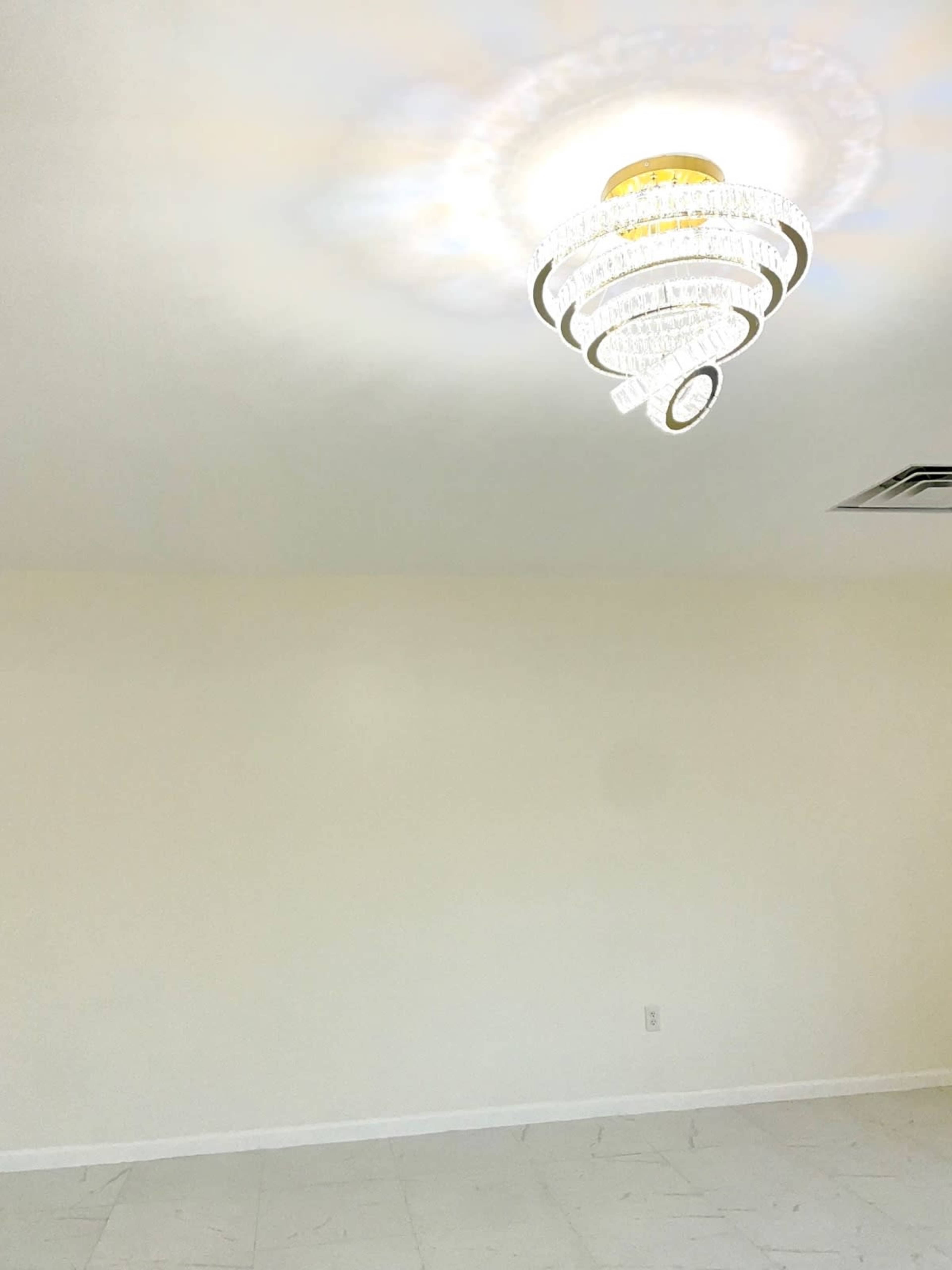 A sparsely furnished room with a modern chandelier mounted on the ceiling and light-colored walls.