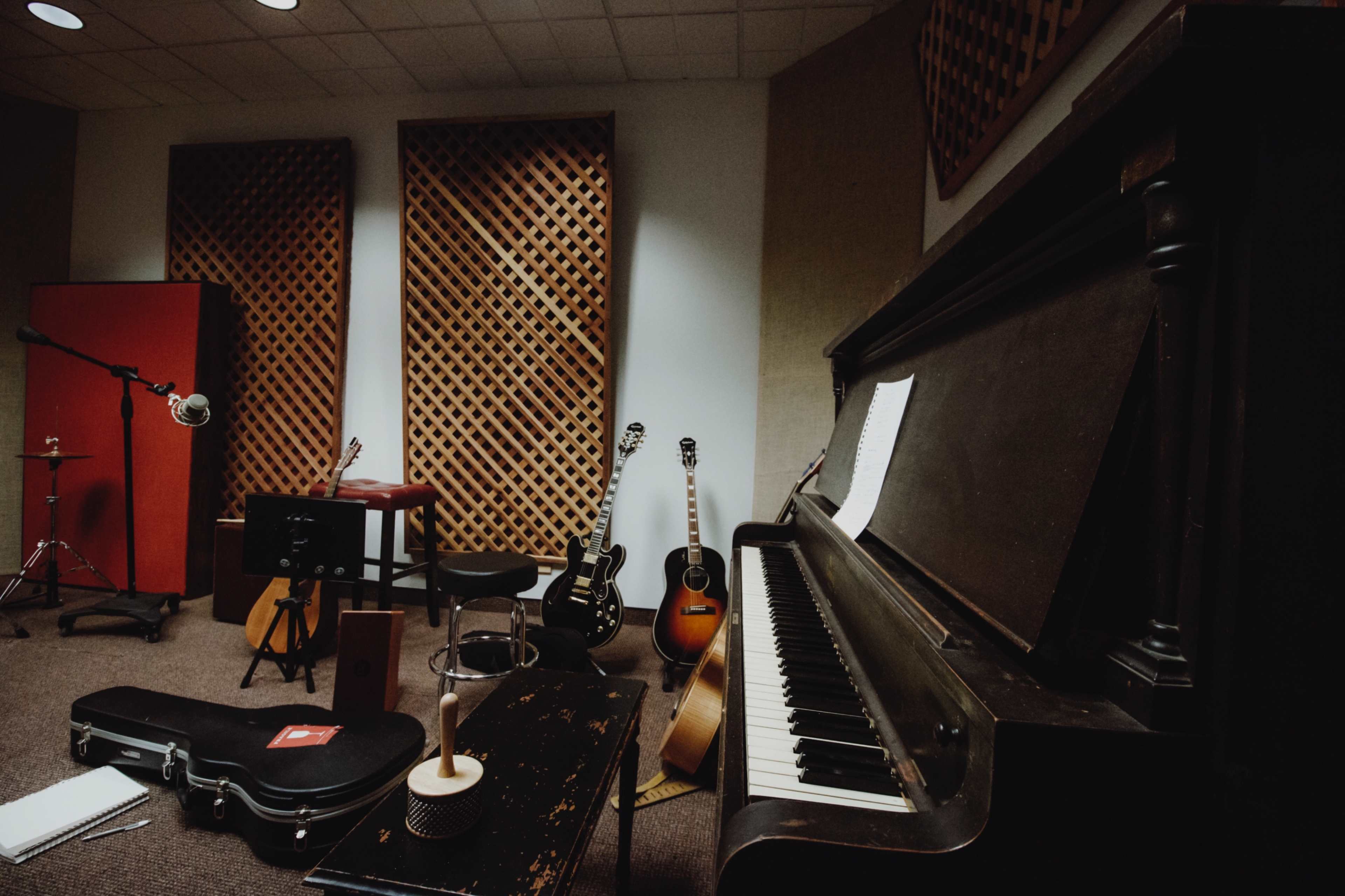 A collection of musical instruments, including a piano, guitars, and a microphone, is arranged in a recording studio setting.