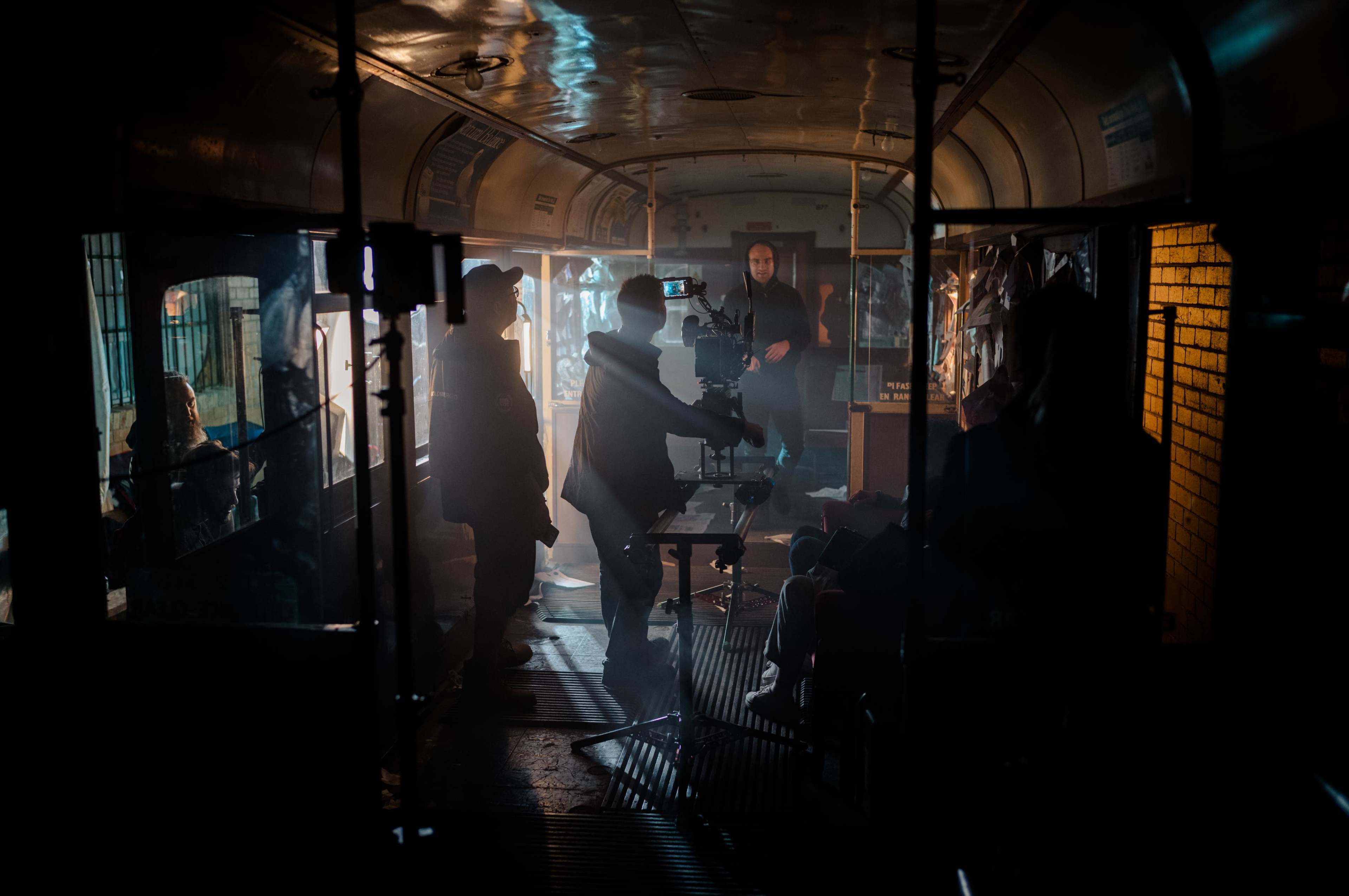 A film crew operates a camera inside a dimly lit vintage bus, capturing a scene with a seated actor.