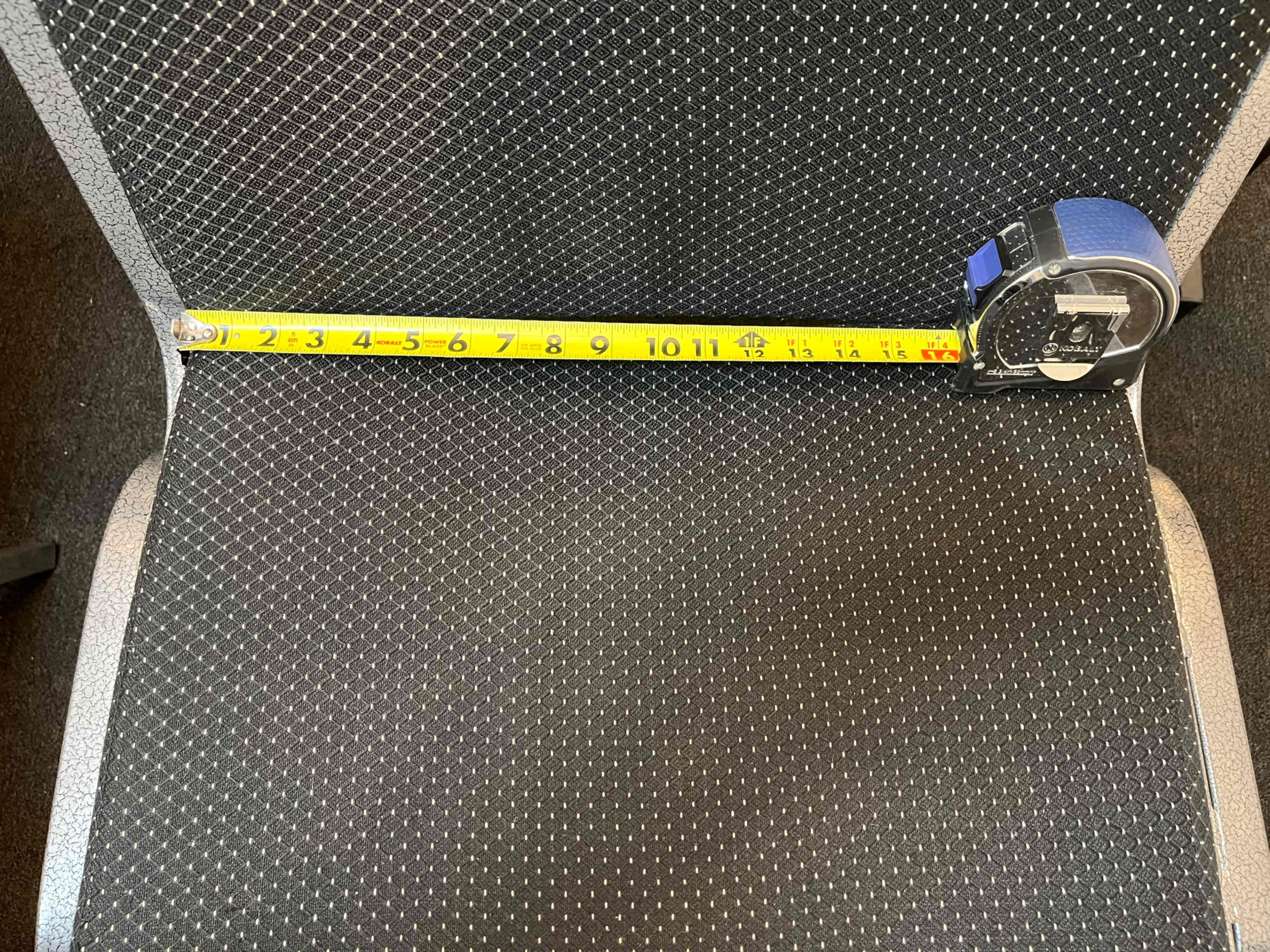 A measuring tape extends across the seat of a black, textured office chair.