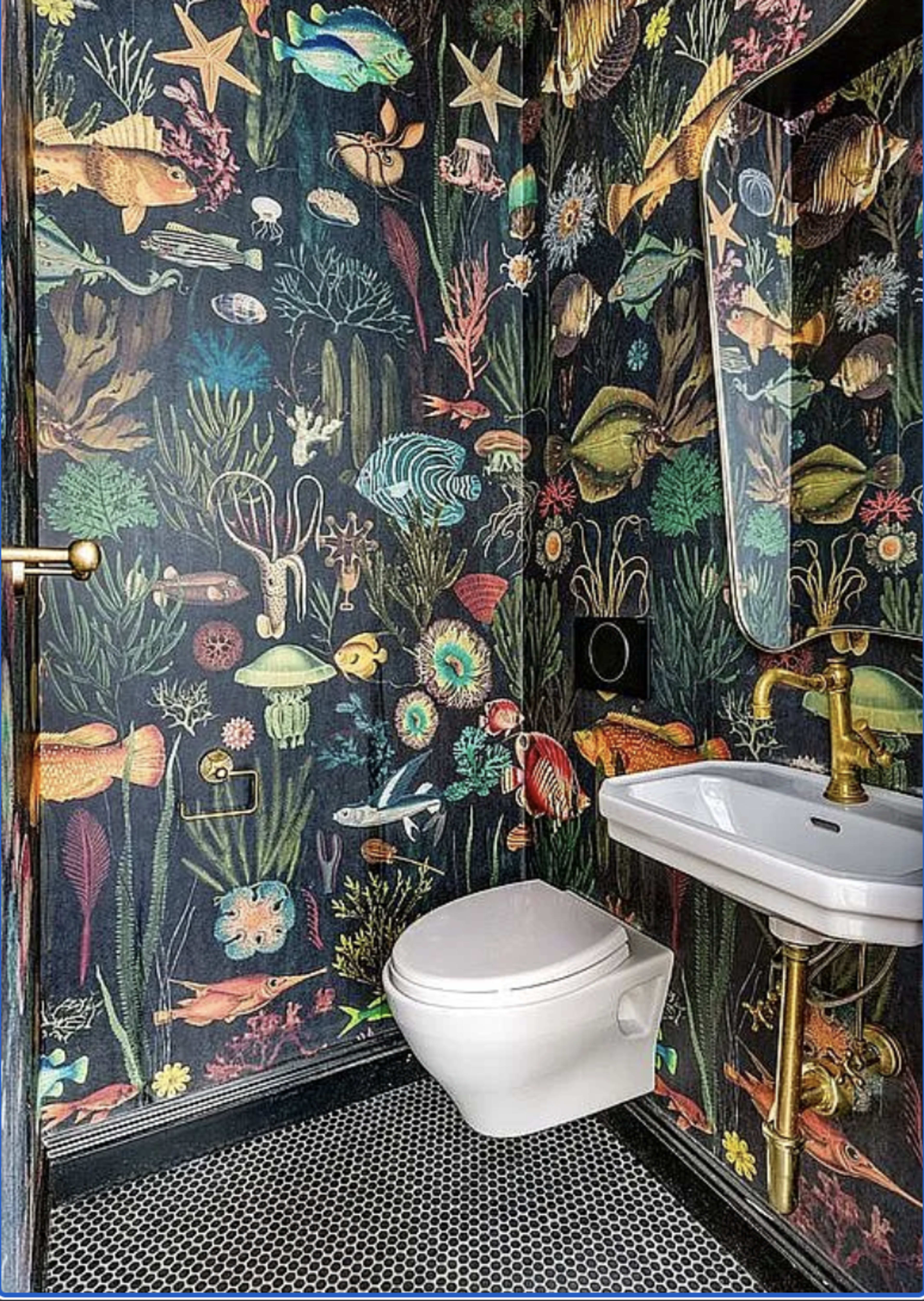 The image depicts a small bathroom with vibrant, ocean-themed wallpaper featuring various marine life, a white toilet, and a simple sink with a brass faucet.