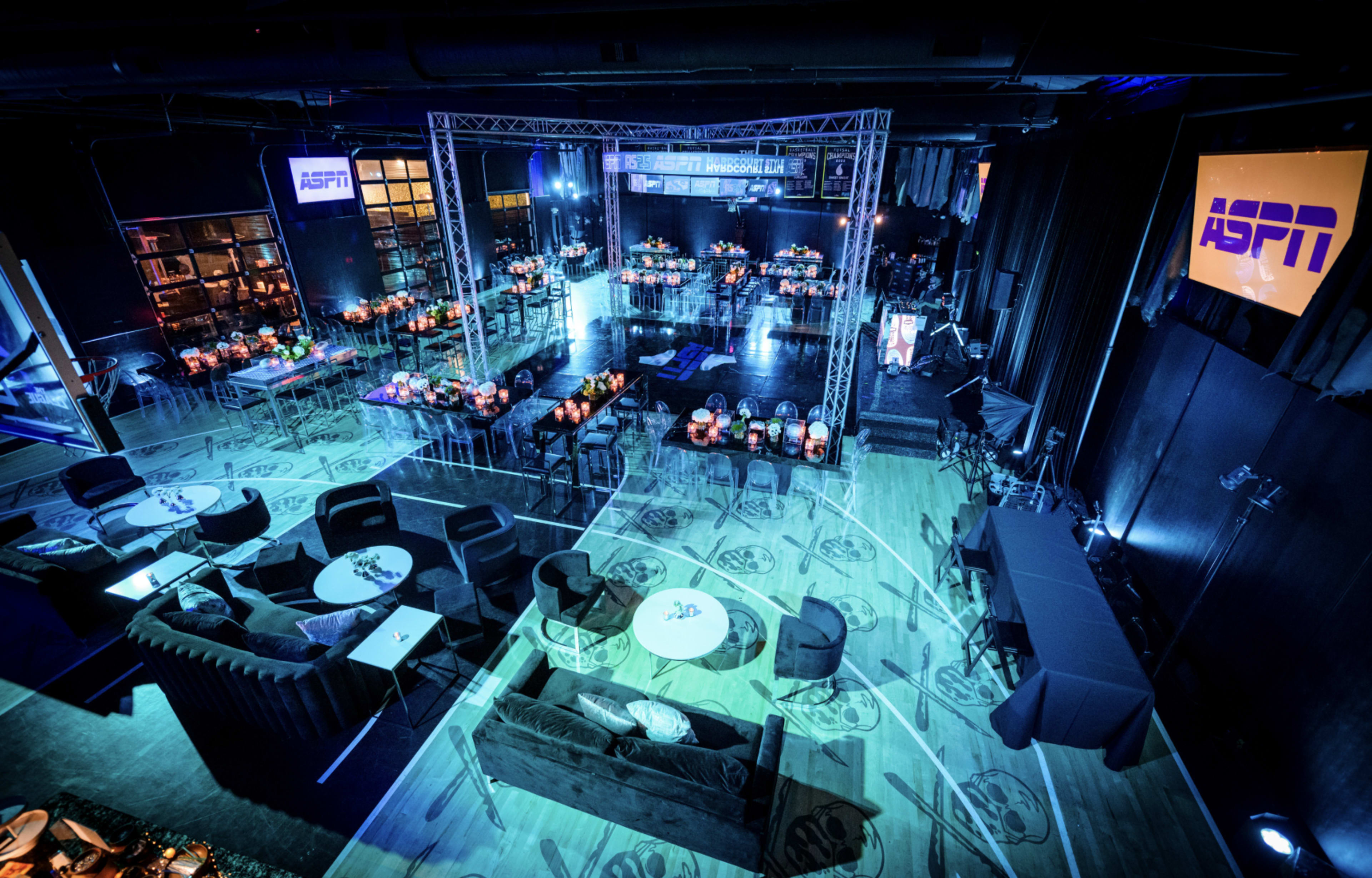 The image shows a spacious event venue set up with tables, chairs, and lighting for a formal gathering.