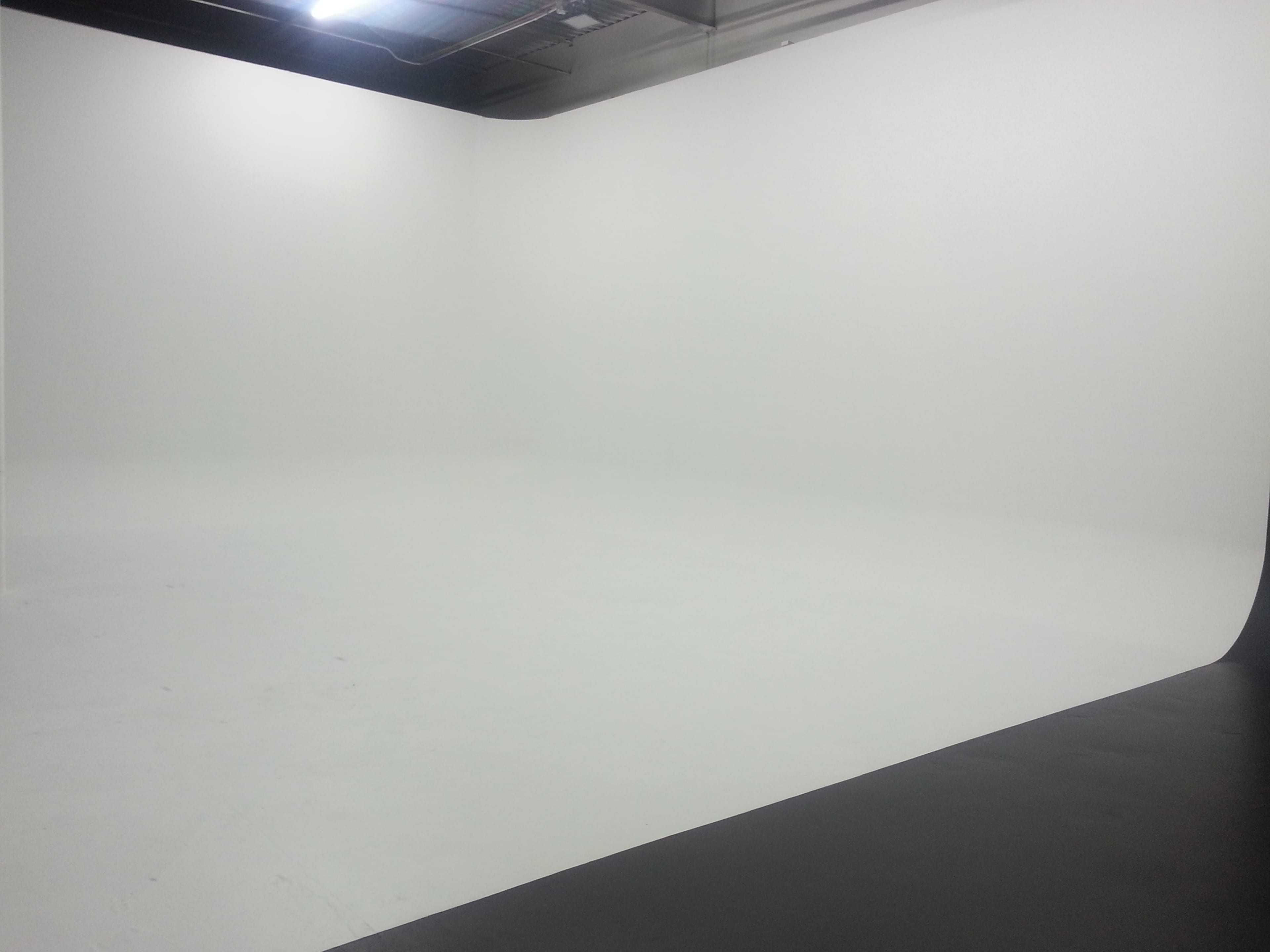 The image shows a spacious, empty studio with white walls and a seamless white floor.
