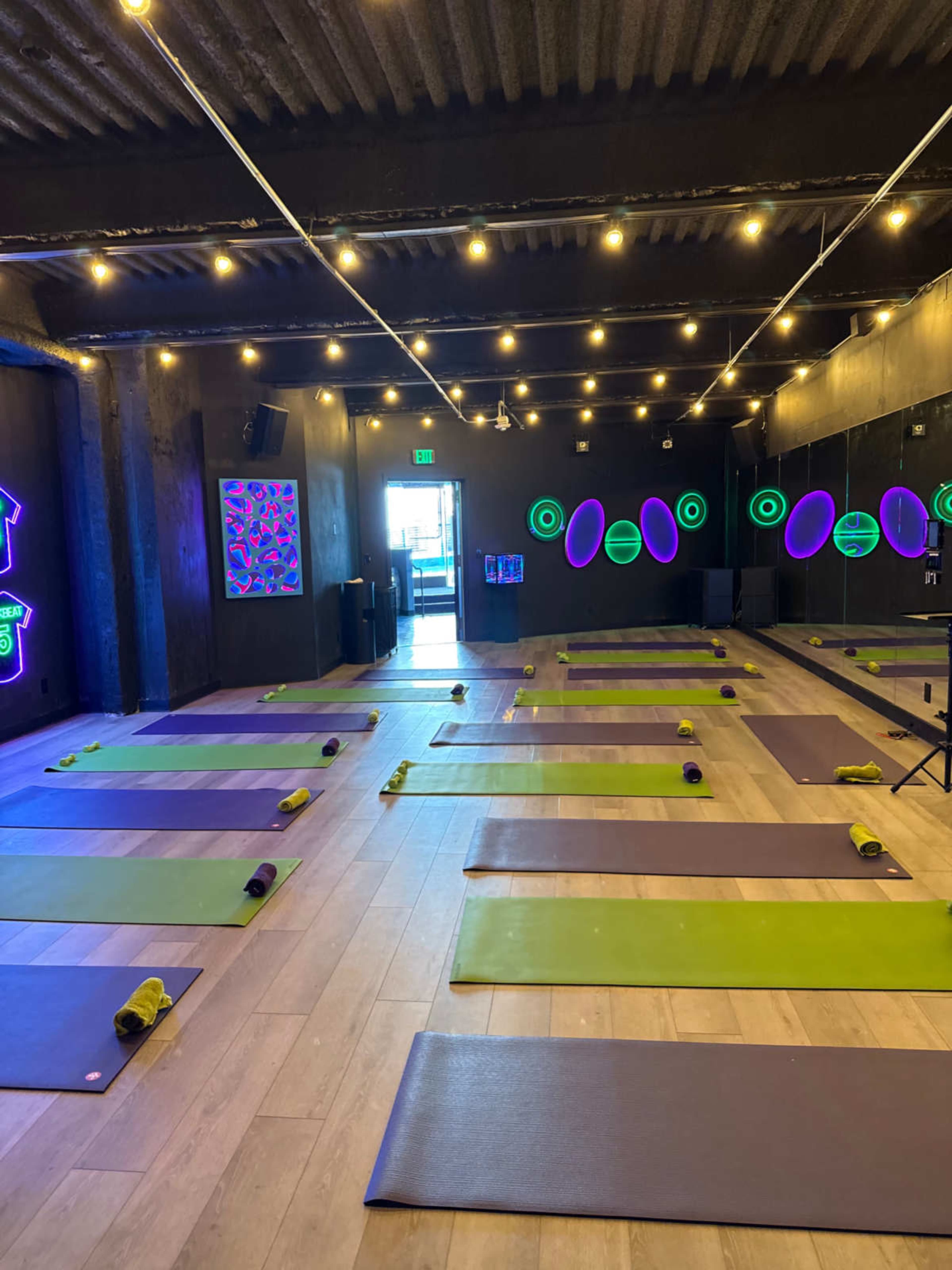 The image shows a yoga studio with multiple yoga mats arranged on the floor and purple lighting illuminating the space.