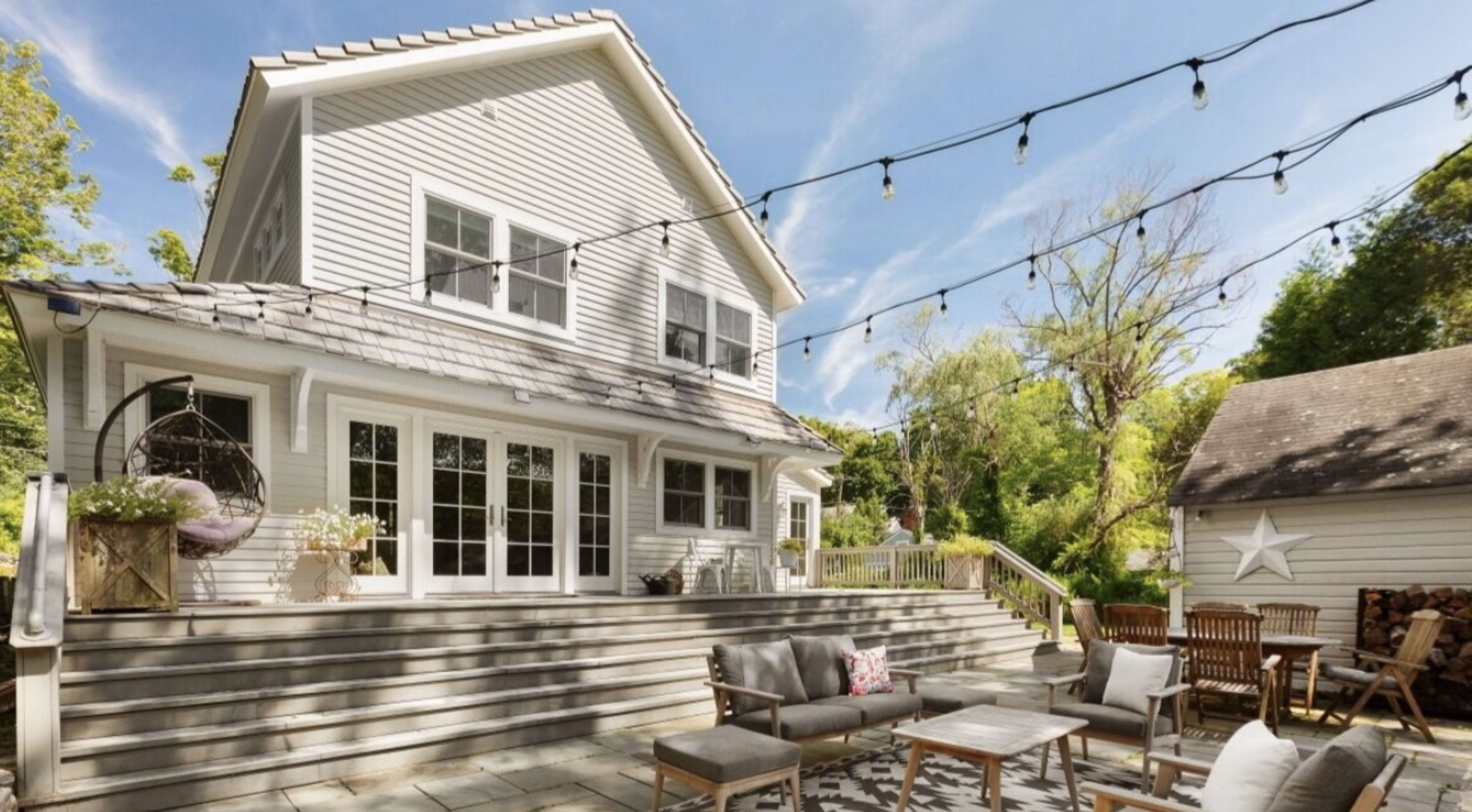 A two-story house with a deck, outdoor seating, and string lights overhead.