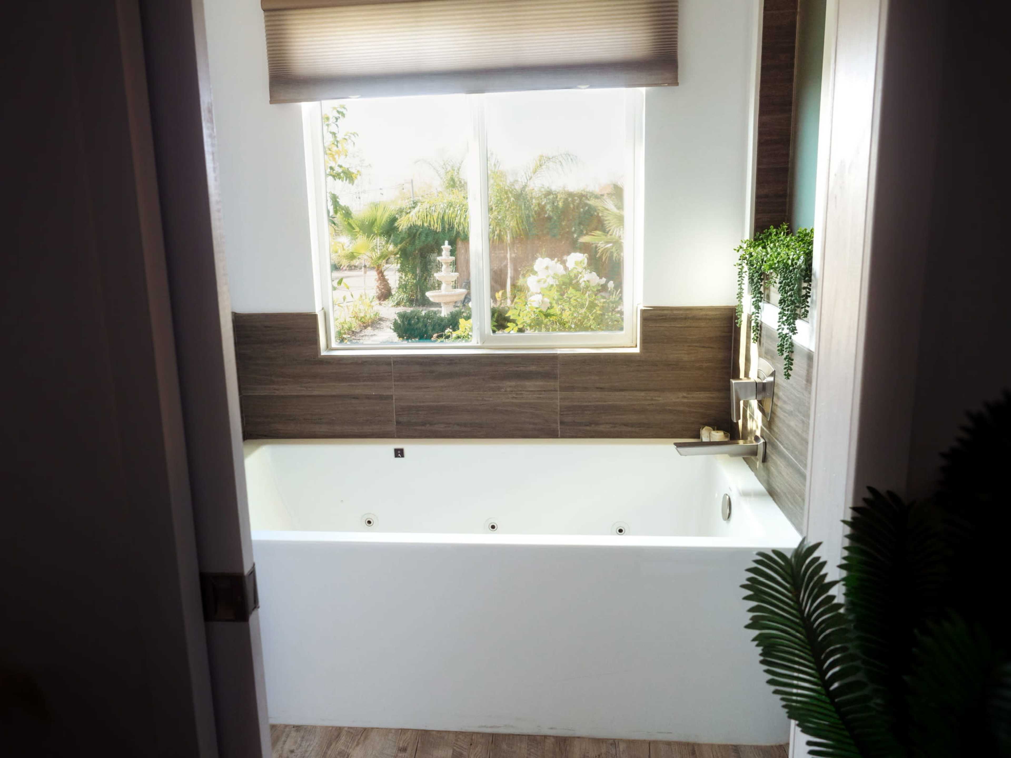 A modern bathroom with a white bathtub underneath a window overlooking a garden with a fountain.