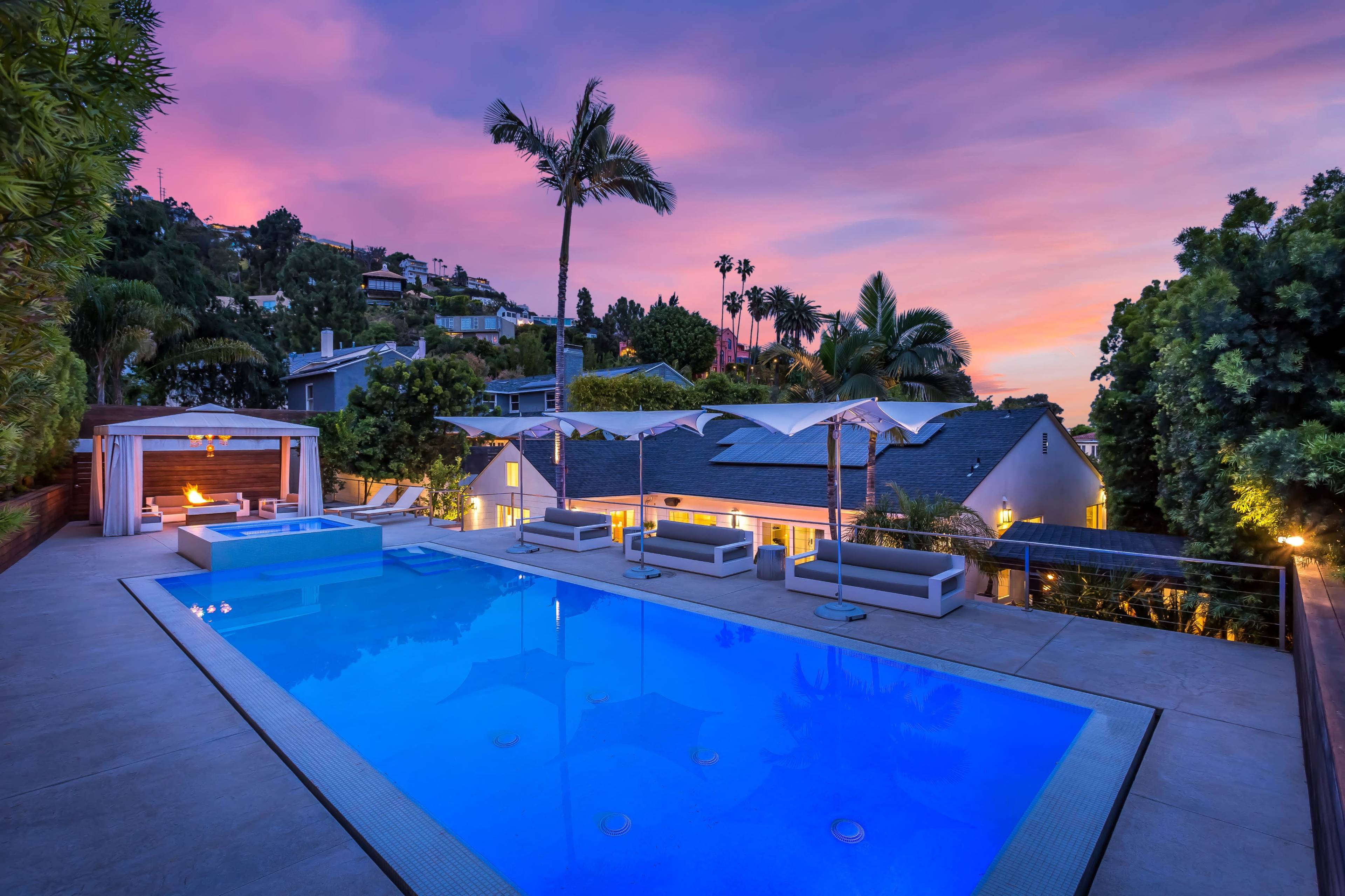 A modern outdoor pool area with lounge seating and a sunset sky in the background.