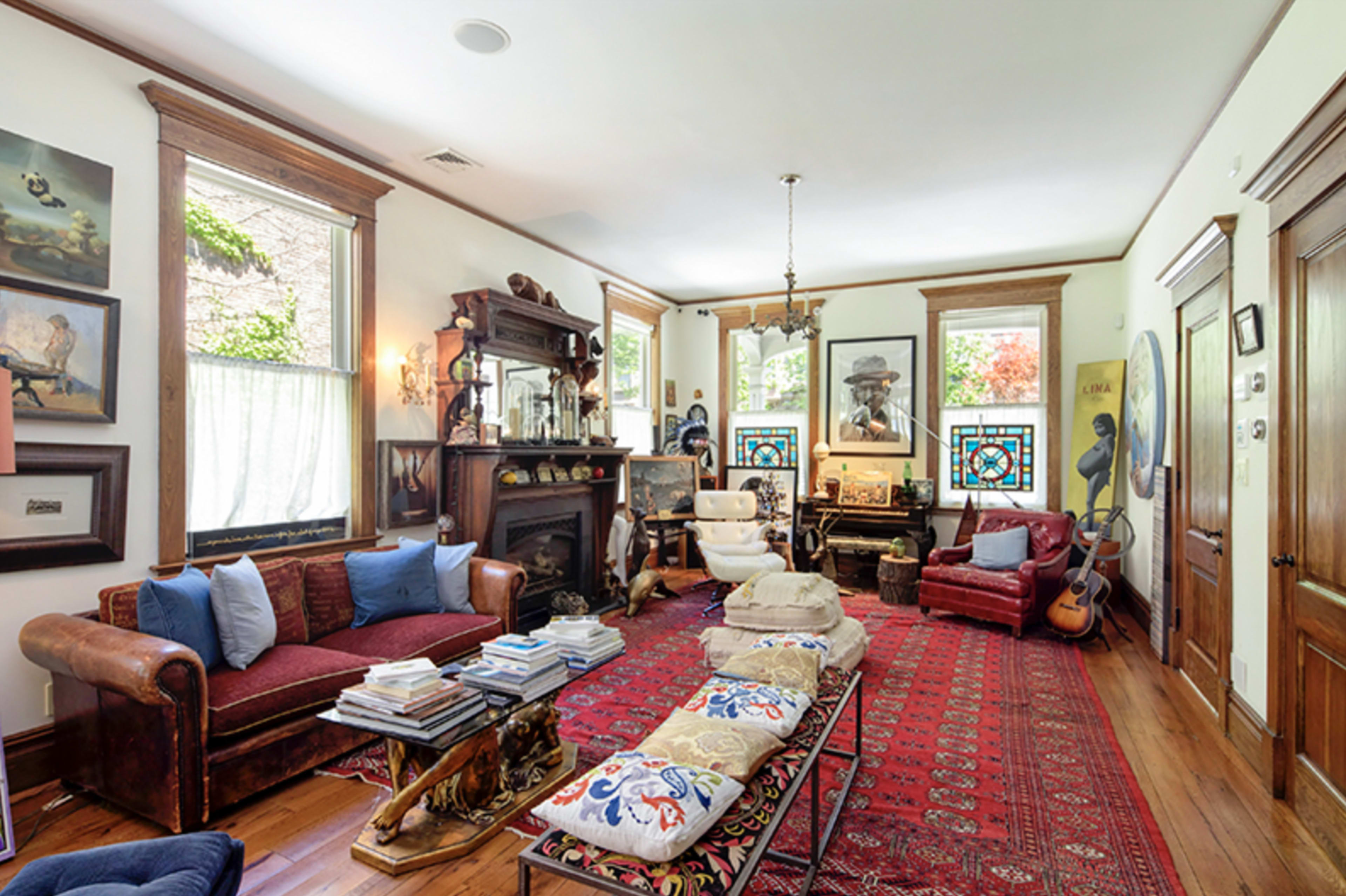 The living room features a mix of vintage furniture, vibrant artwork, and a large patterned rug on polished wooden floors.