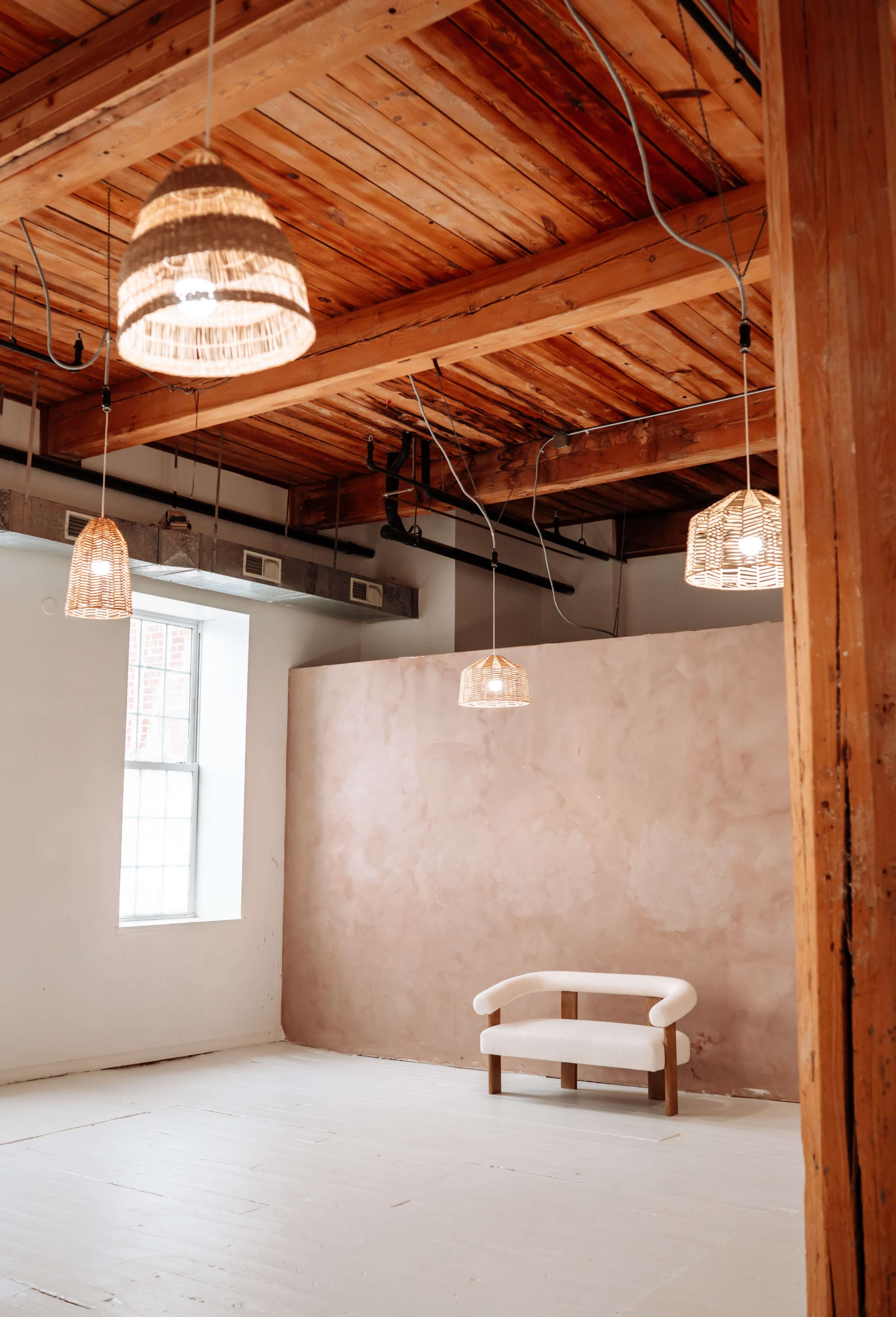 The scene features a spacious room with wooden beams and pendant lights hanging from the ceiling, centered around a minimalist white sofa against a textured wall.