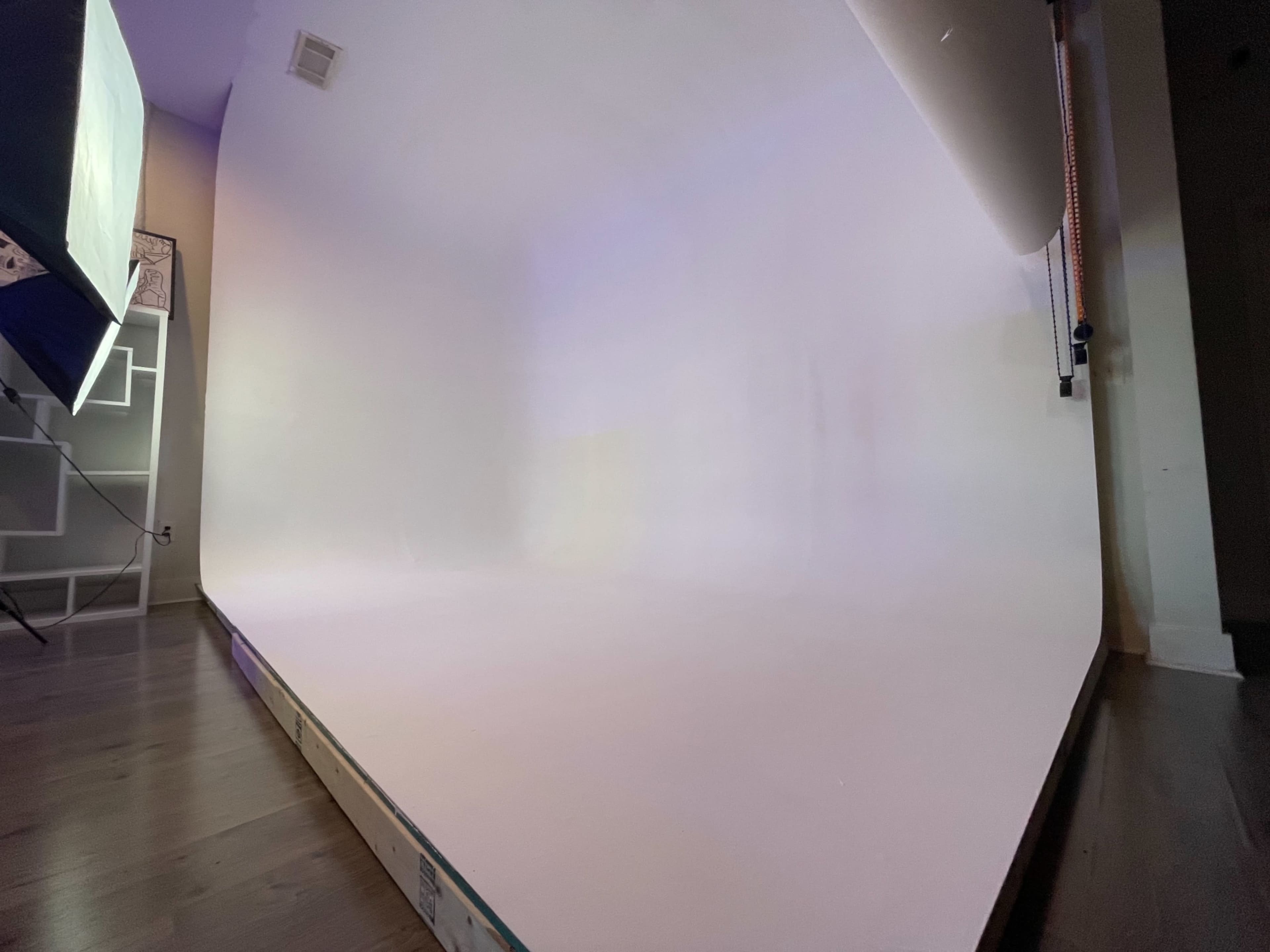 A corner of a photography studio featuring a seamless white backdrop and wooden flooring.