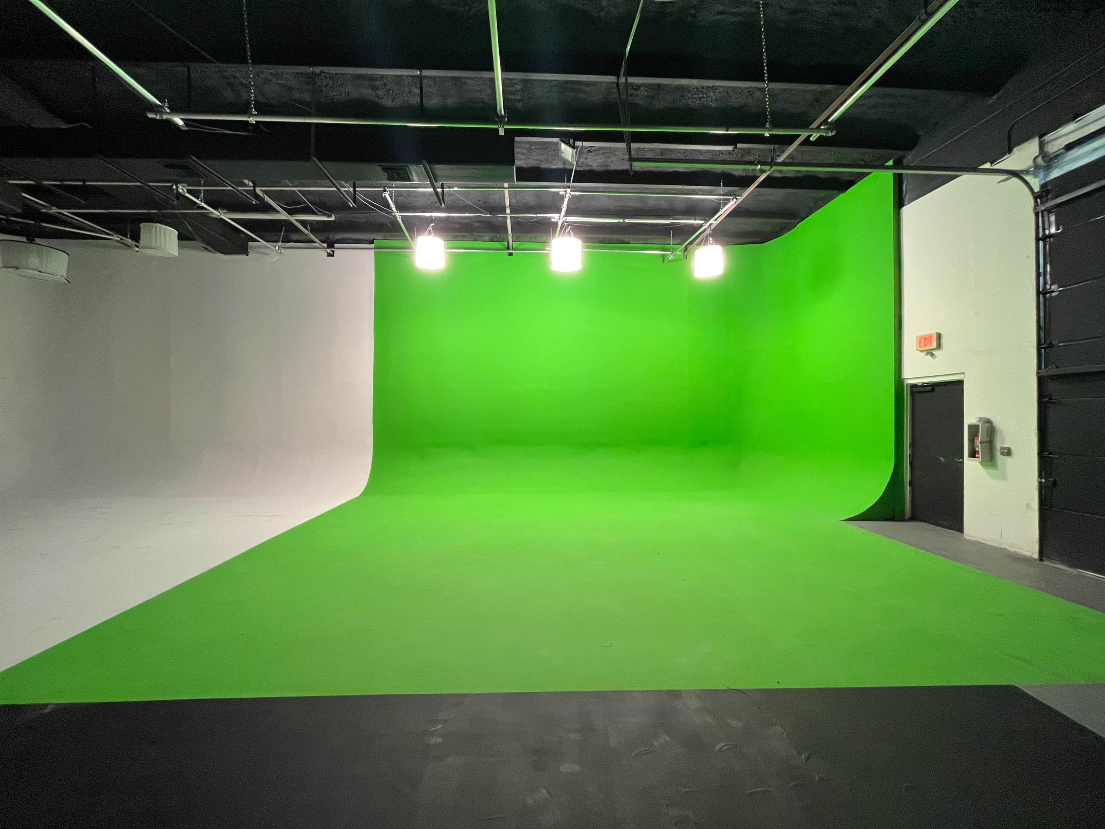 A spacious studio with a green screen backdrop on one side and a white backdrop on the other.
