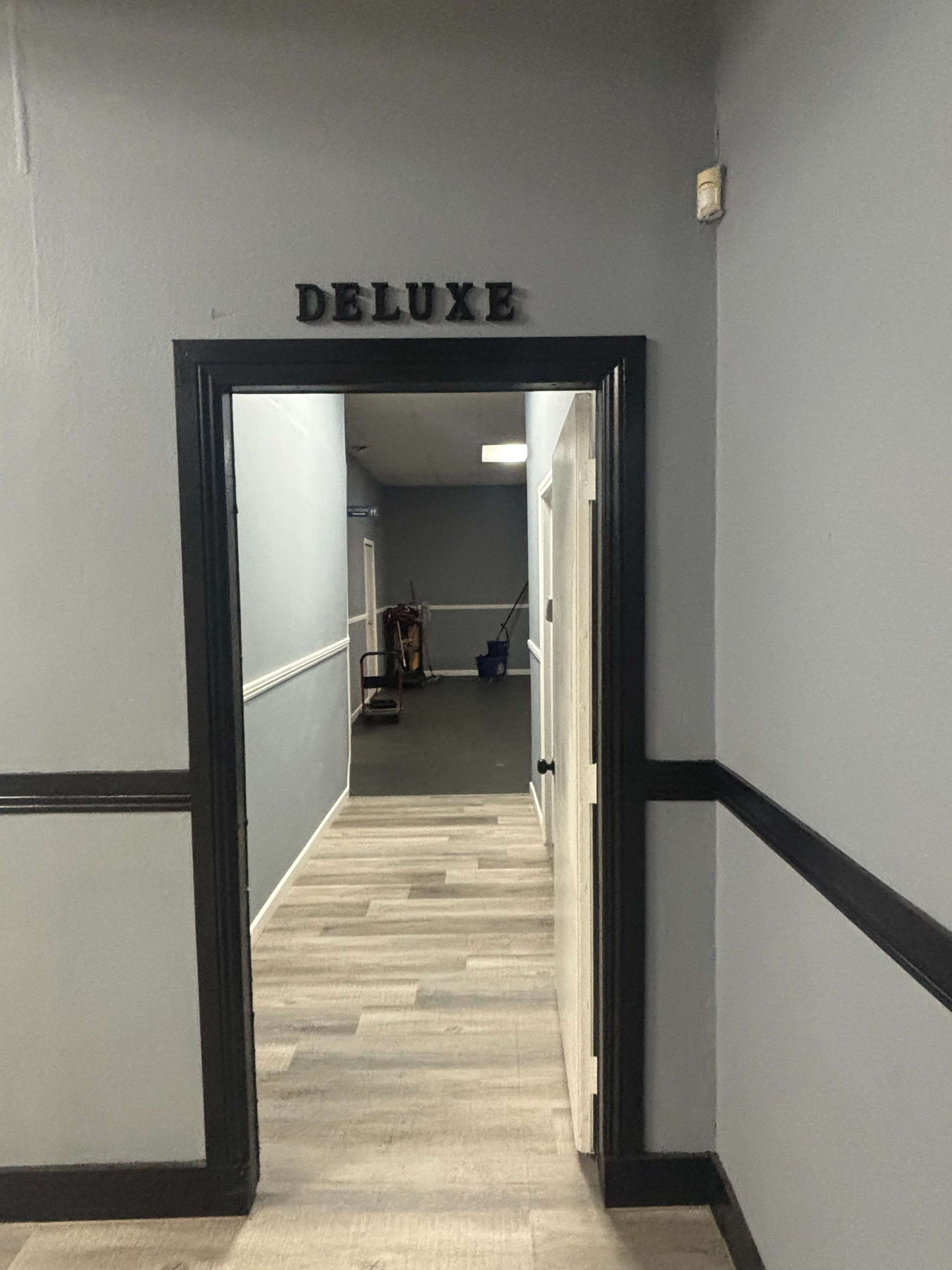 A hallway is visible with a sign labeling the entrance as "DELUXE," and the walls are painted in a muted color with a contrasting dark trim.