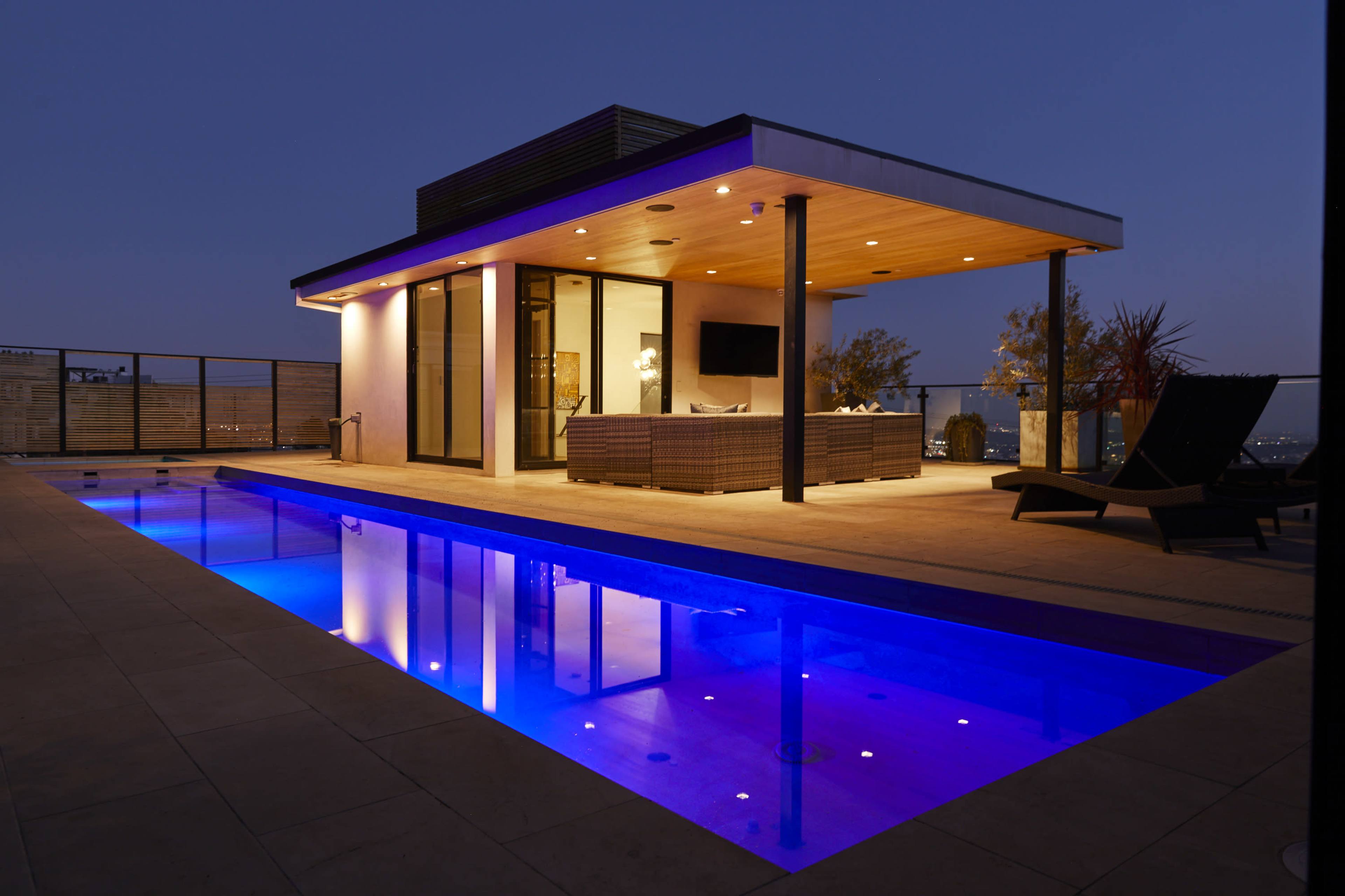A modern building features a pool illuminated with blue lights, reflecting its contemporary architecture against a twilight sky.