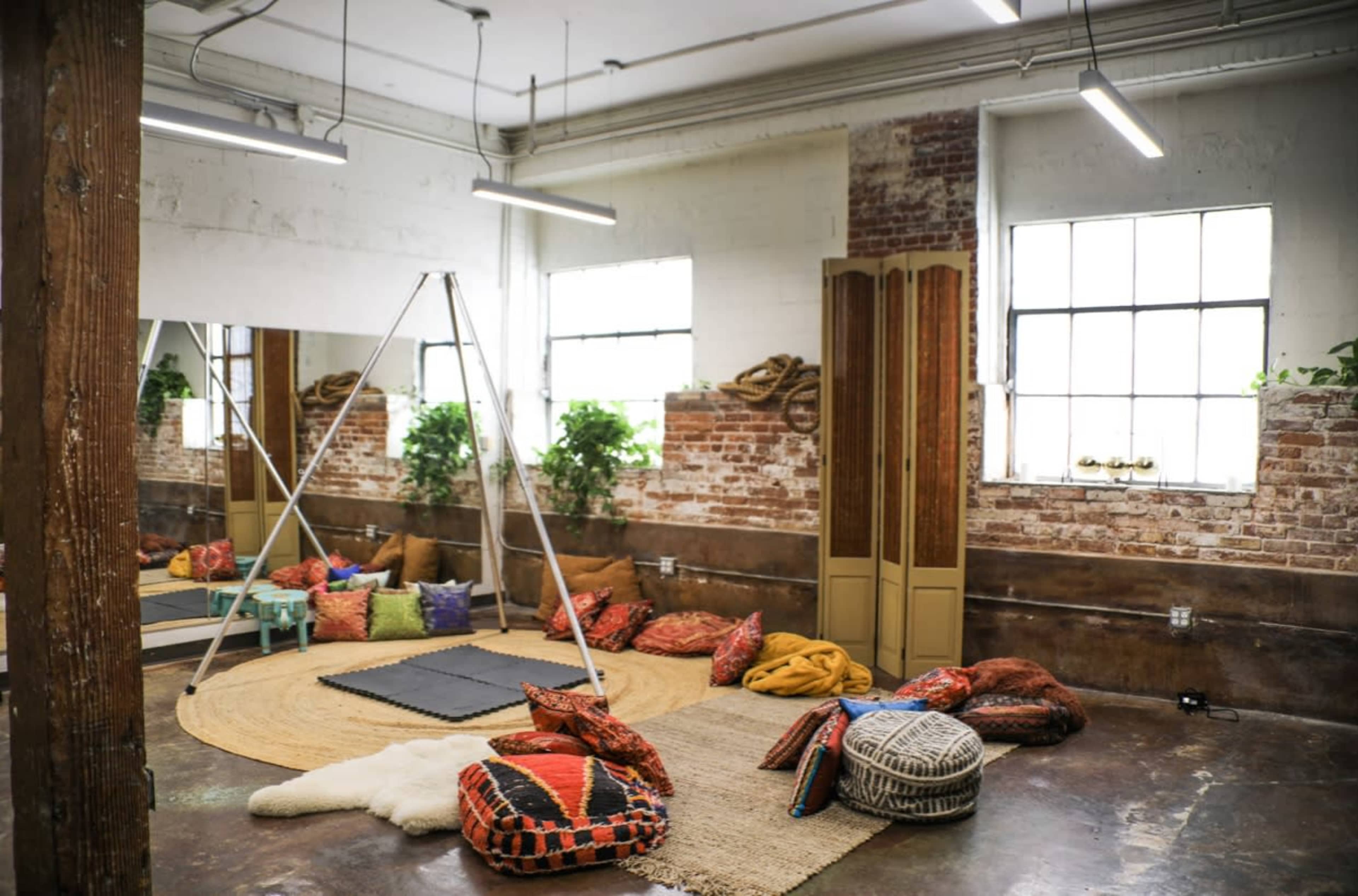 A spacious room with brick walls, large windows, a circular area rug, and various colorful cushions scattered around.