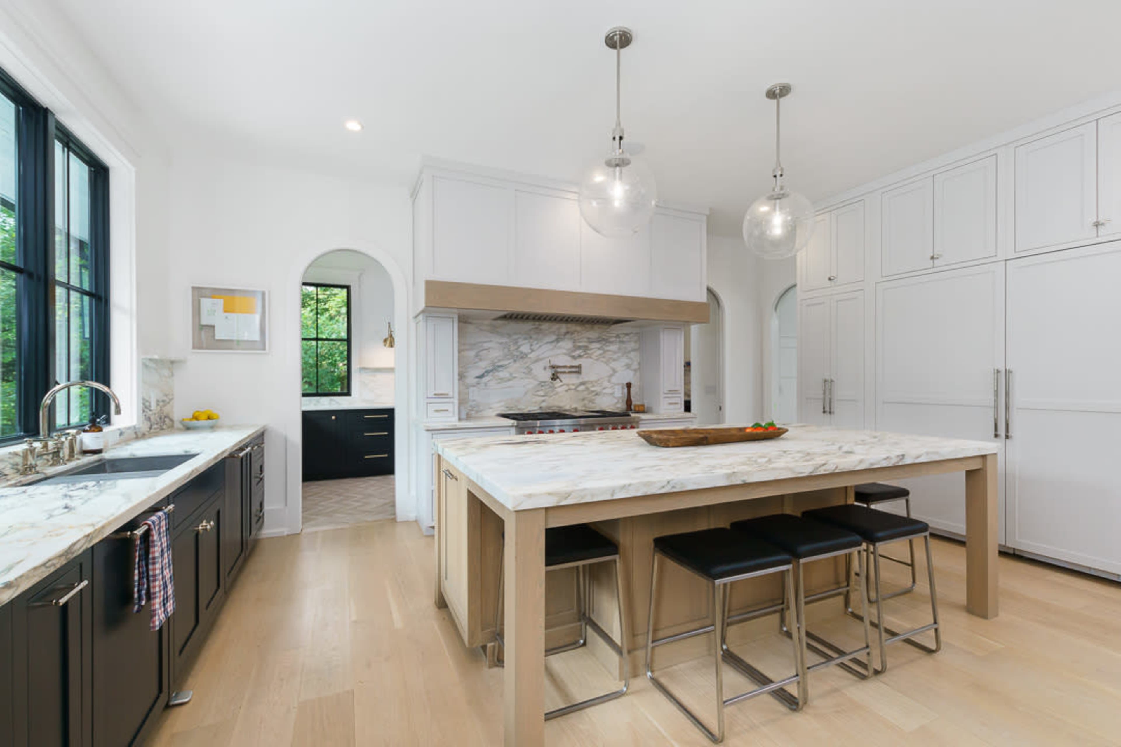 A modern kitchen features a central island with a marble countertop, stainless steel appliances, and a combination of dark cabinetry and light wood flooring.