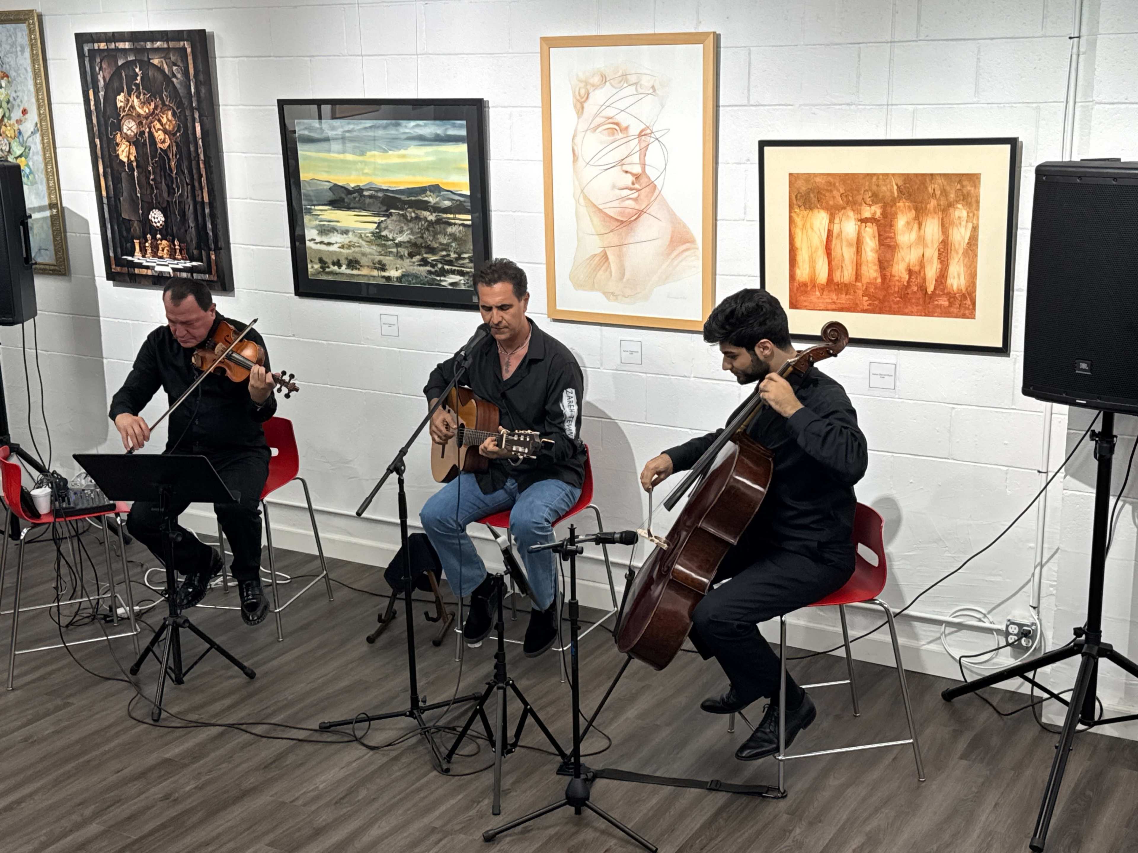 A musician sings while accompanied by a violinist and a cellist in an art gallery.