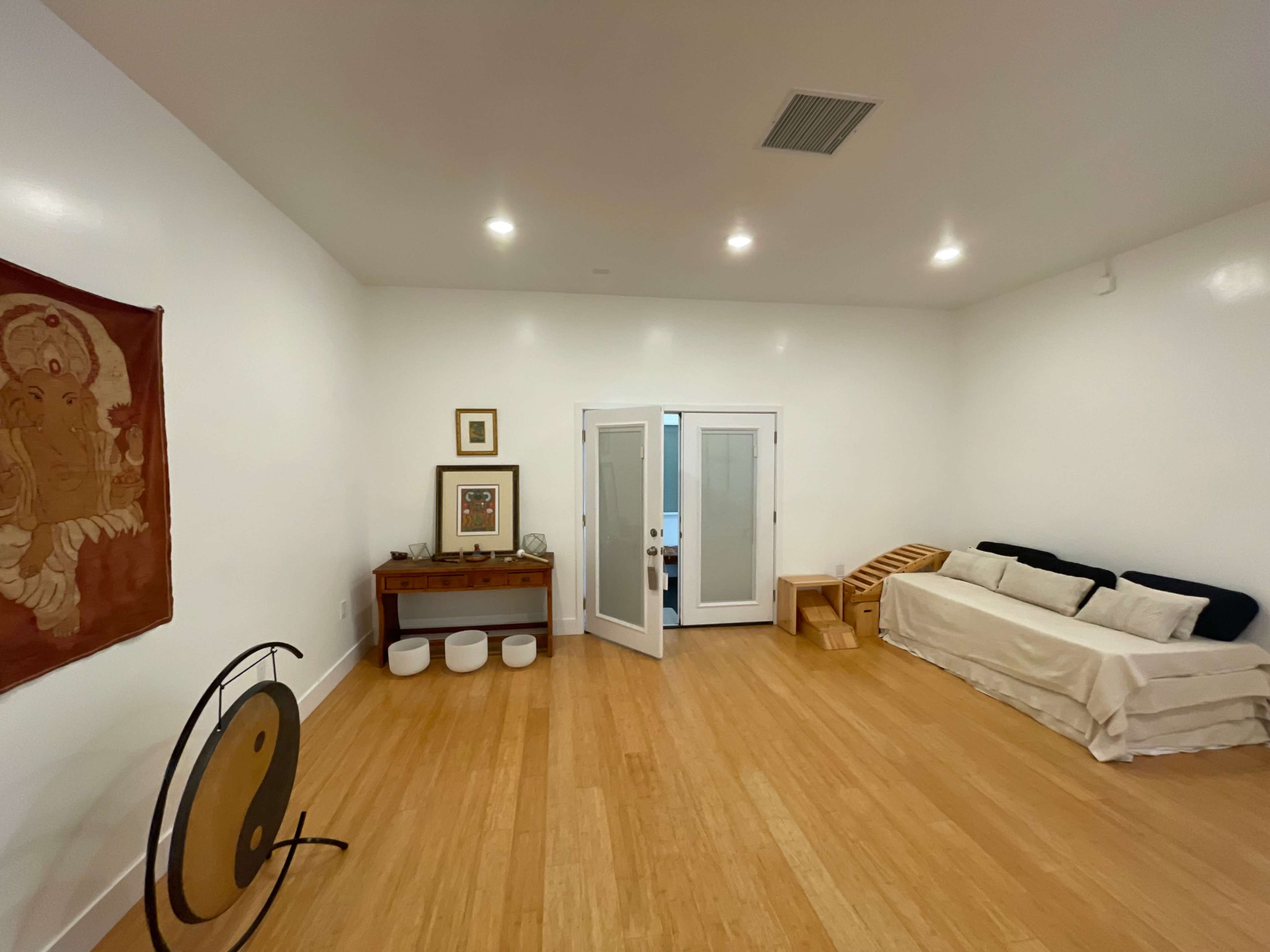 A spacious, brightly lit room with bamboo flooring, featuring a large sofa, a wooden table, and several decorative items along the walls.