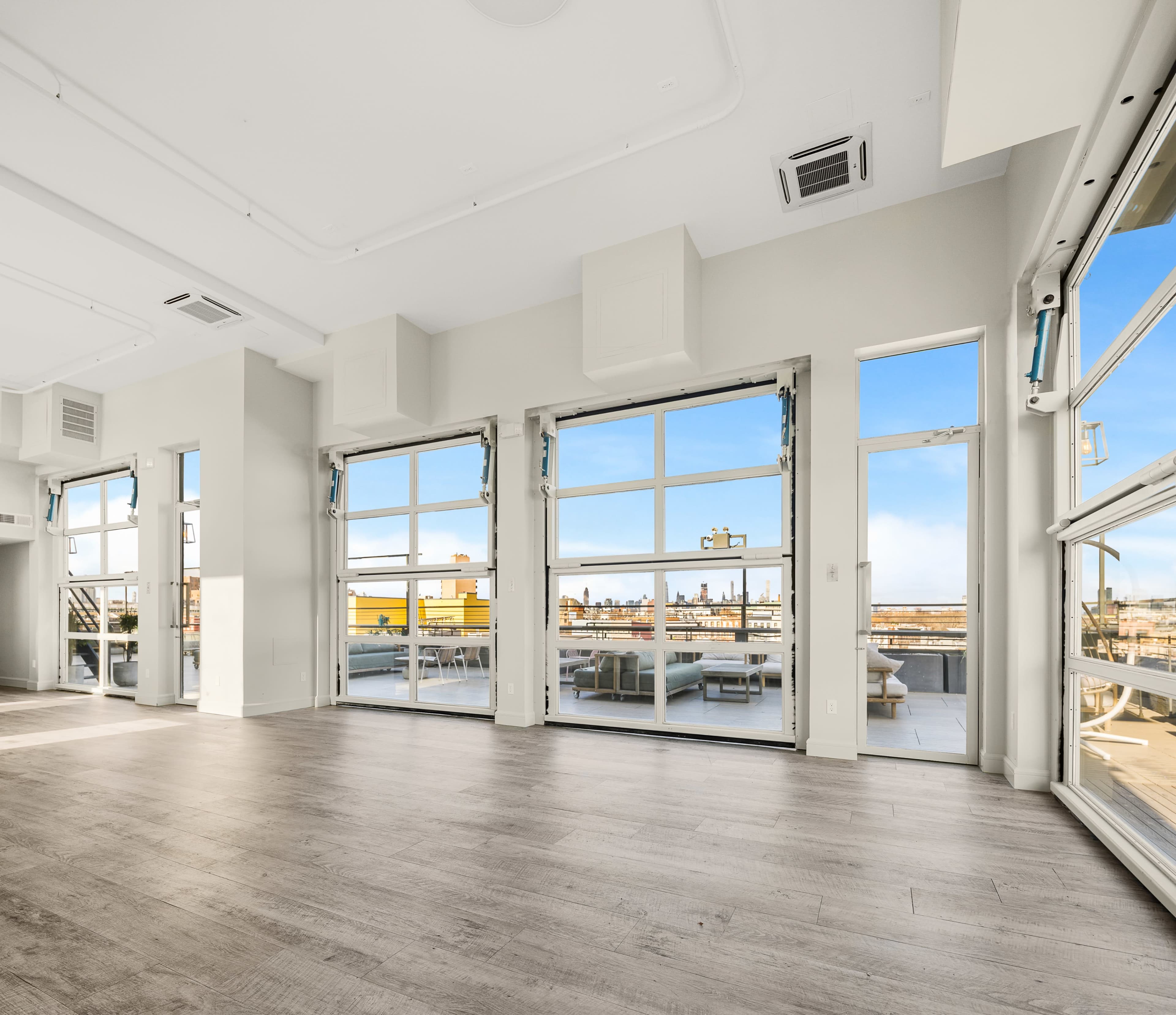 A spacious, modern interior with large windows and doors that open to a balcony, offering a view of the skyline.