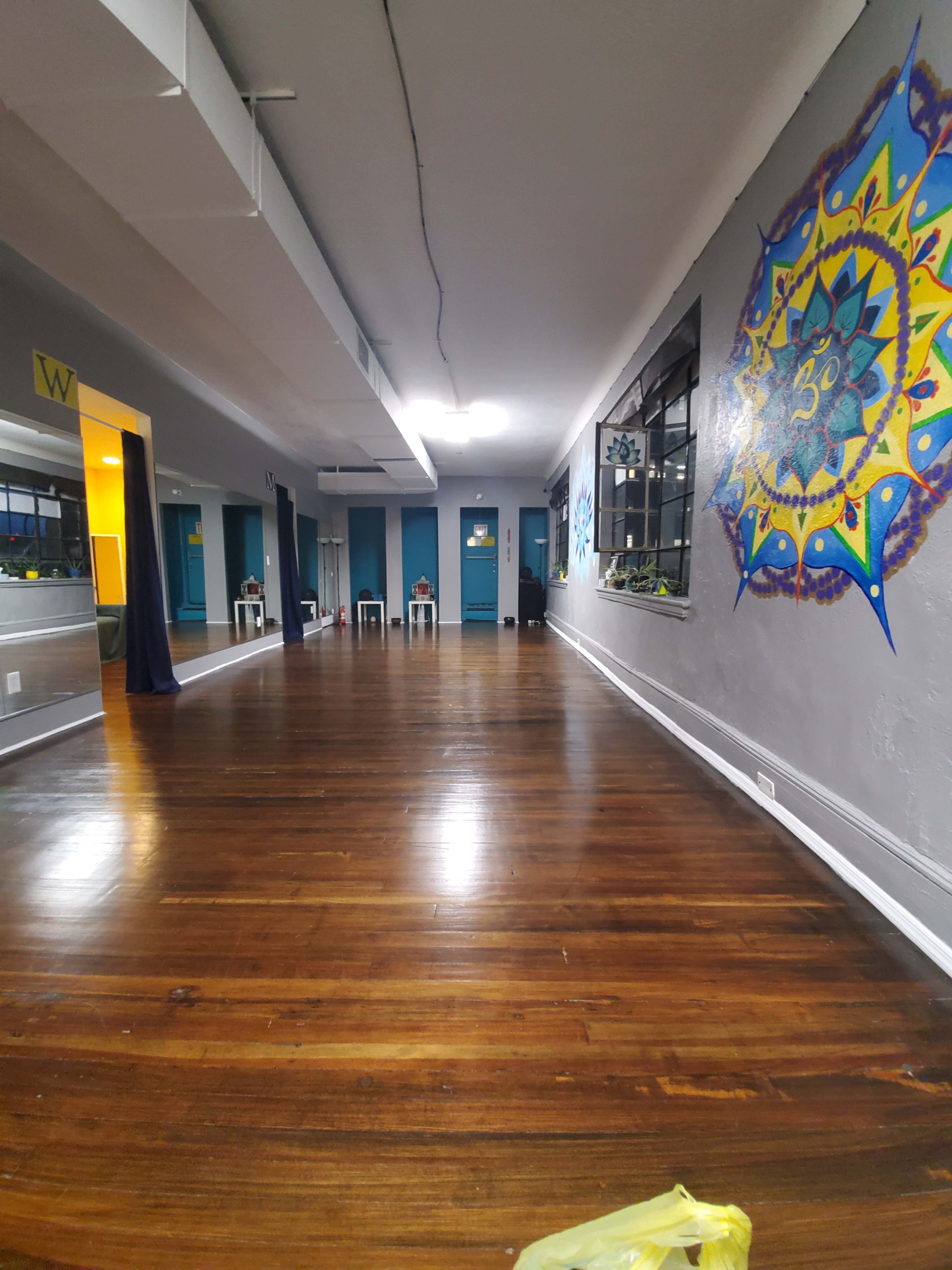 An empty dance studio with polished wooden floors and blue walls adorned with colorful artwork.