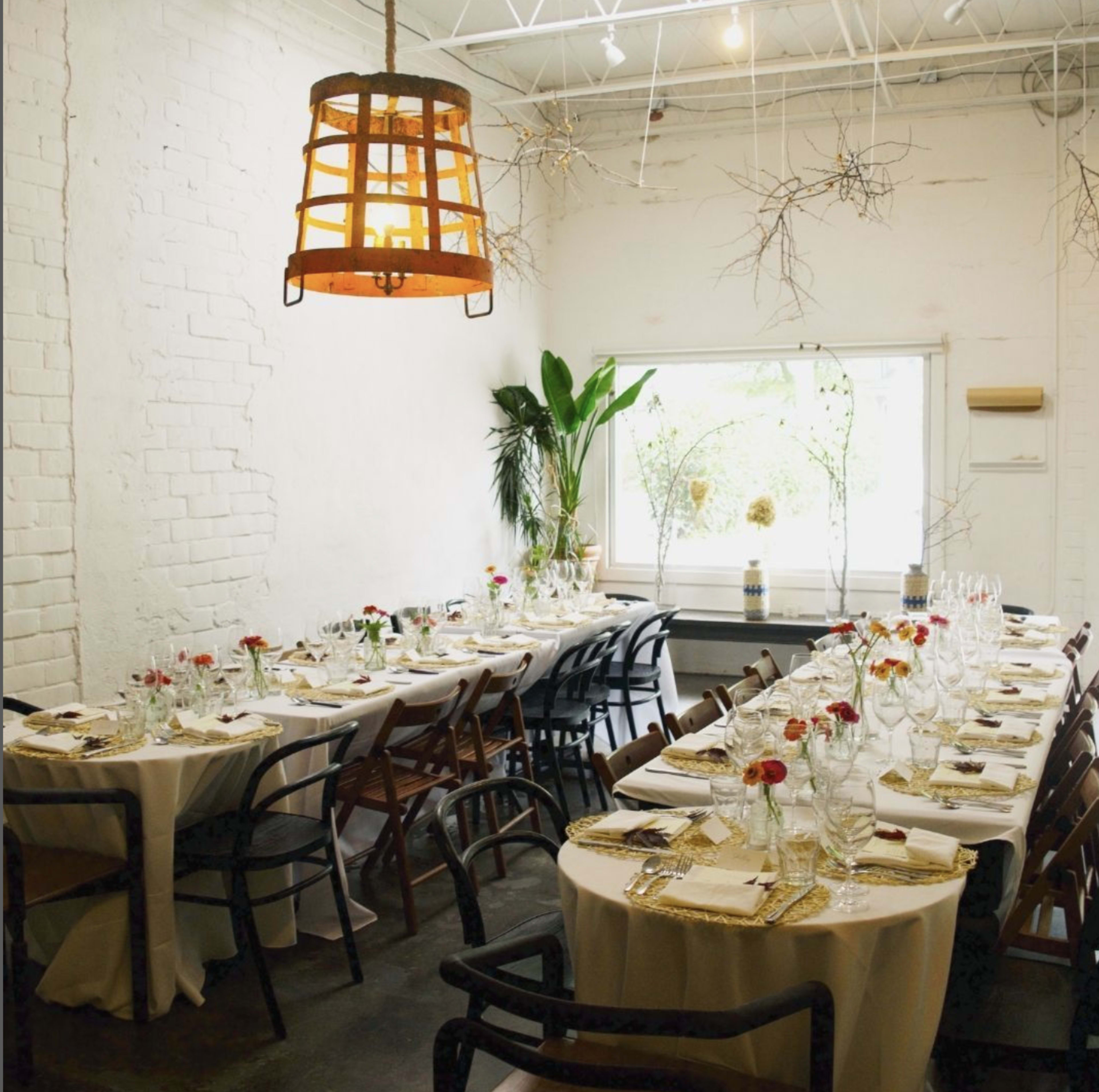 A spacious dining area features elegantly set tables with white tablecloths and floral centerpieces, illuminated by a hanging lantern above.