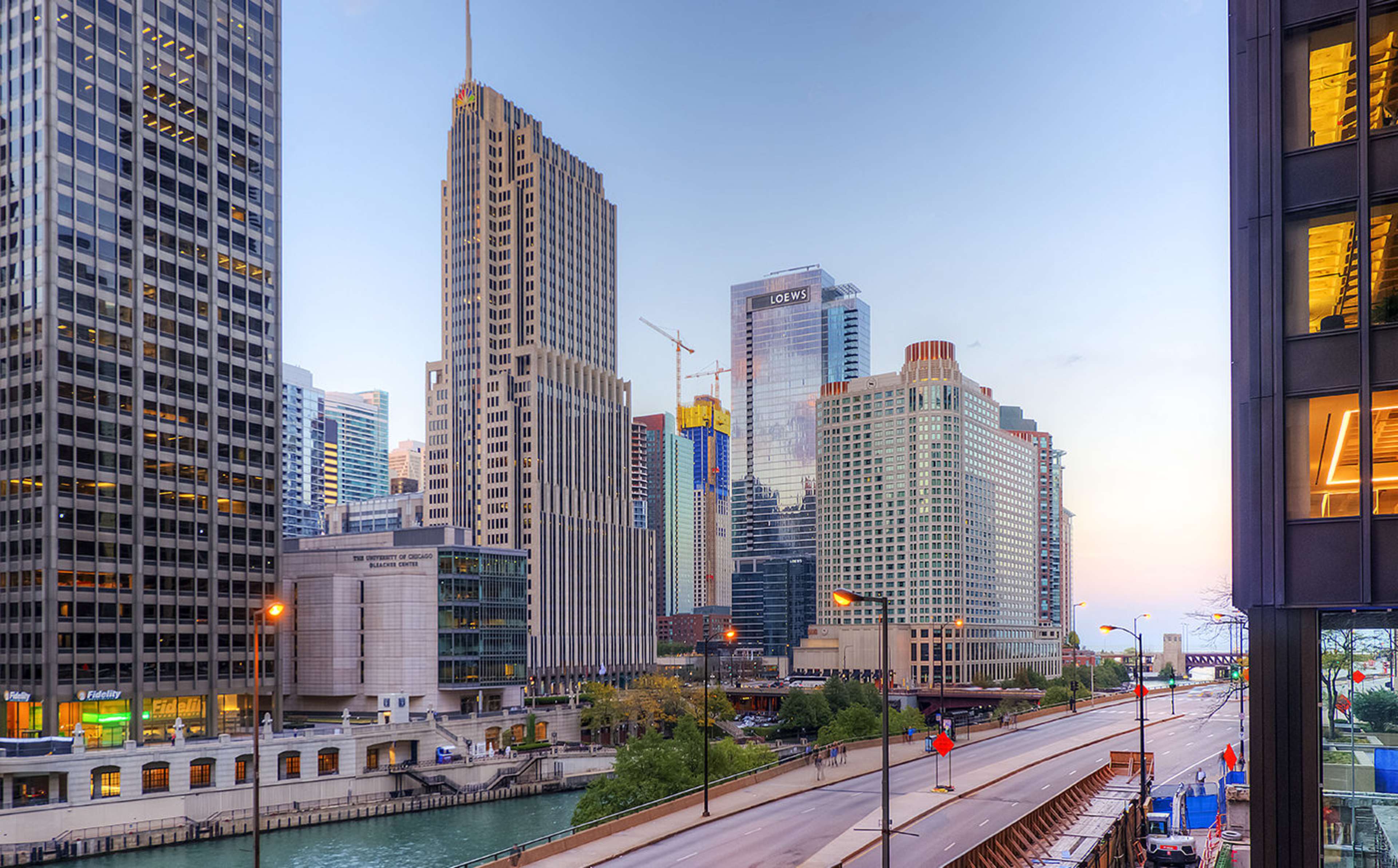 A cityscape of downtown Chicago featuring tall buildings along the river with a wide street in the foreground.