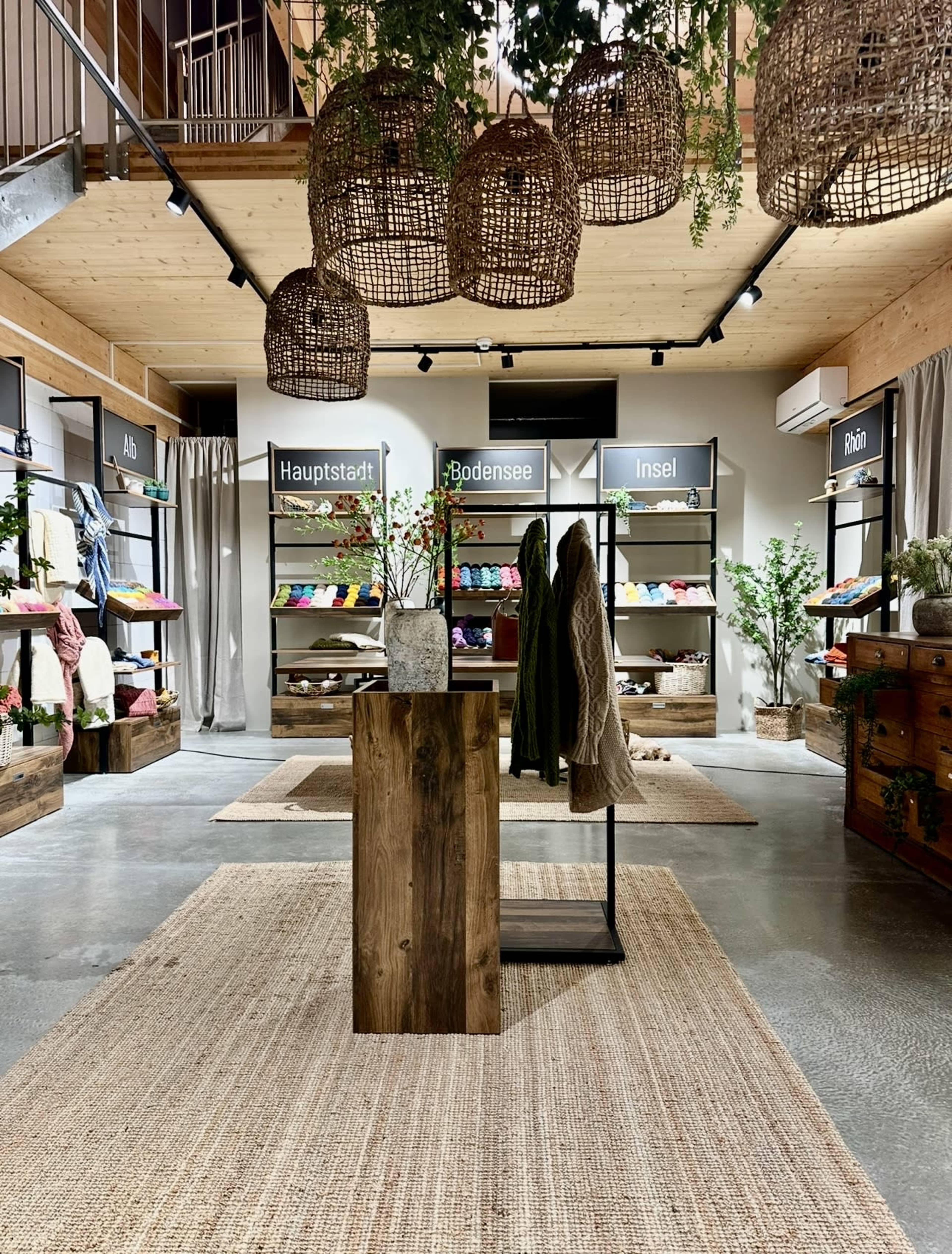 The image shows a retail space featuring wooden displays, clothing racks with colorful apparel, and pendant lights, all set against a minimalist interior design.