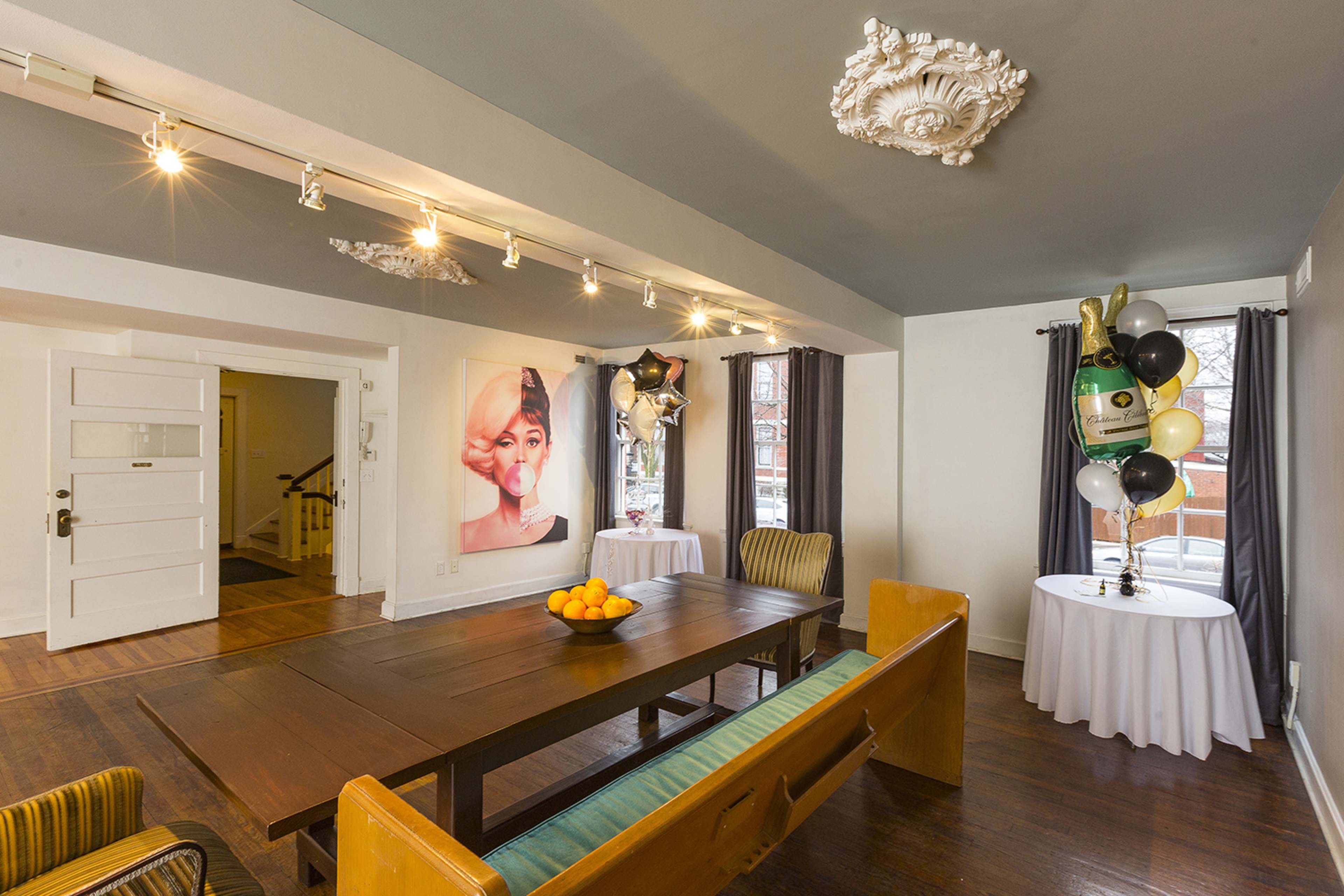 A spacious room with a wooden dining table, a large portrait on the wall, and decorations for a celebration in one corner.