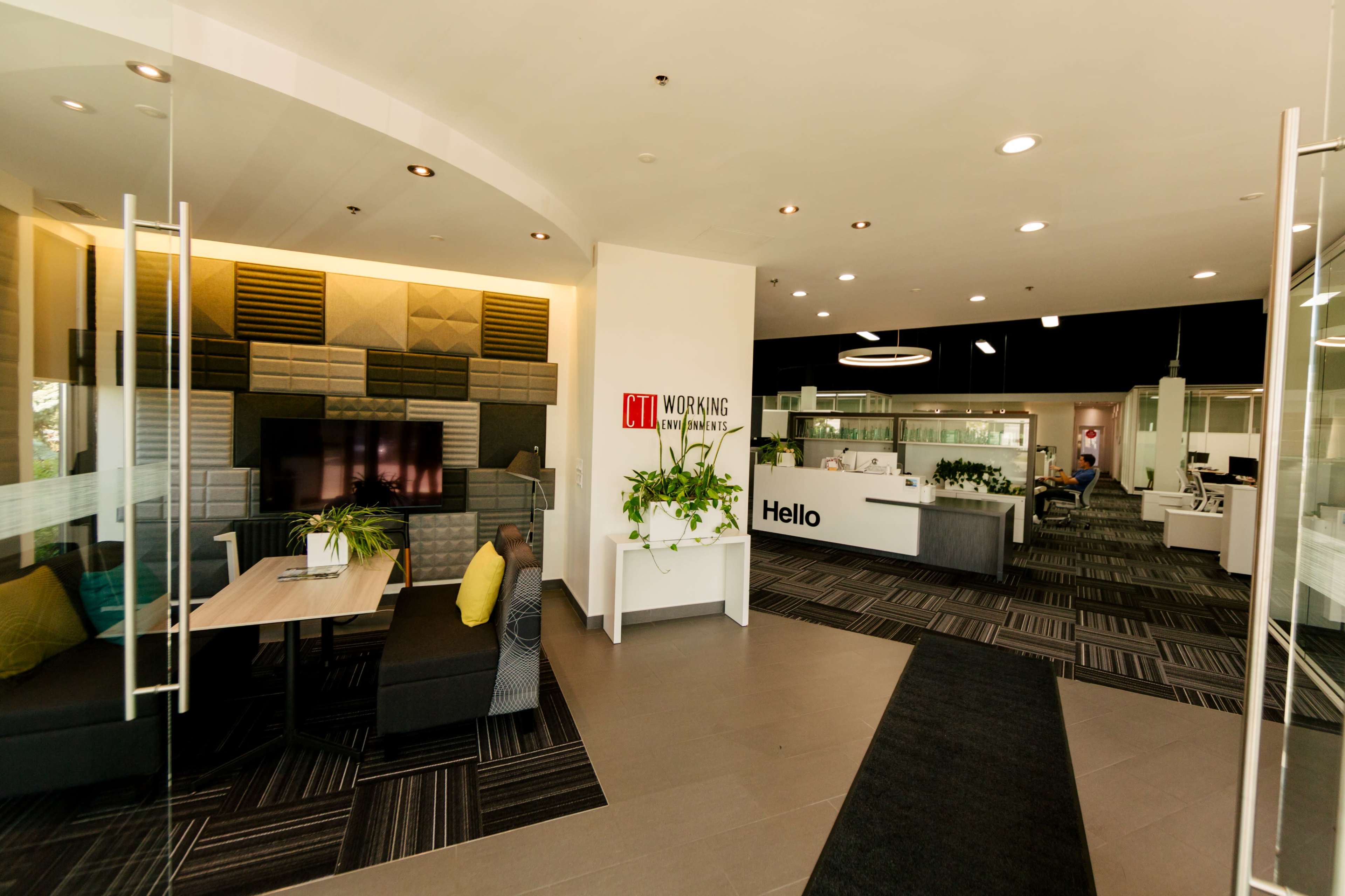 The image depicts a modern office lobby with a reception area, comfortable seating, and a large communal workspace.
