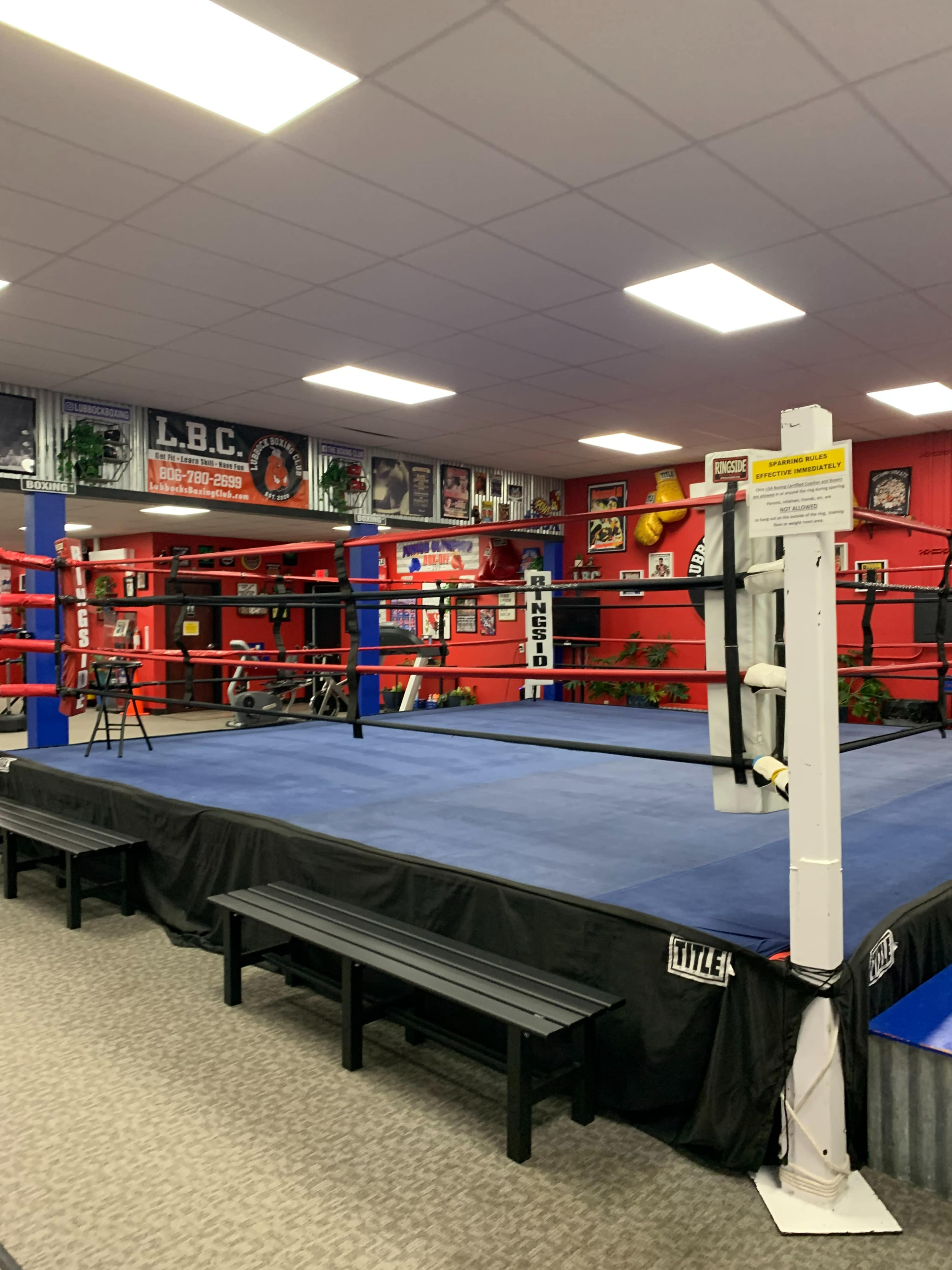 A boxing ring surrounded by benches and fitness equipment in a brightly decorated gym.