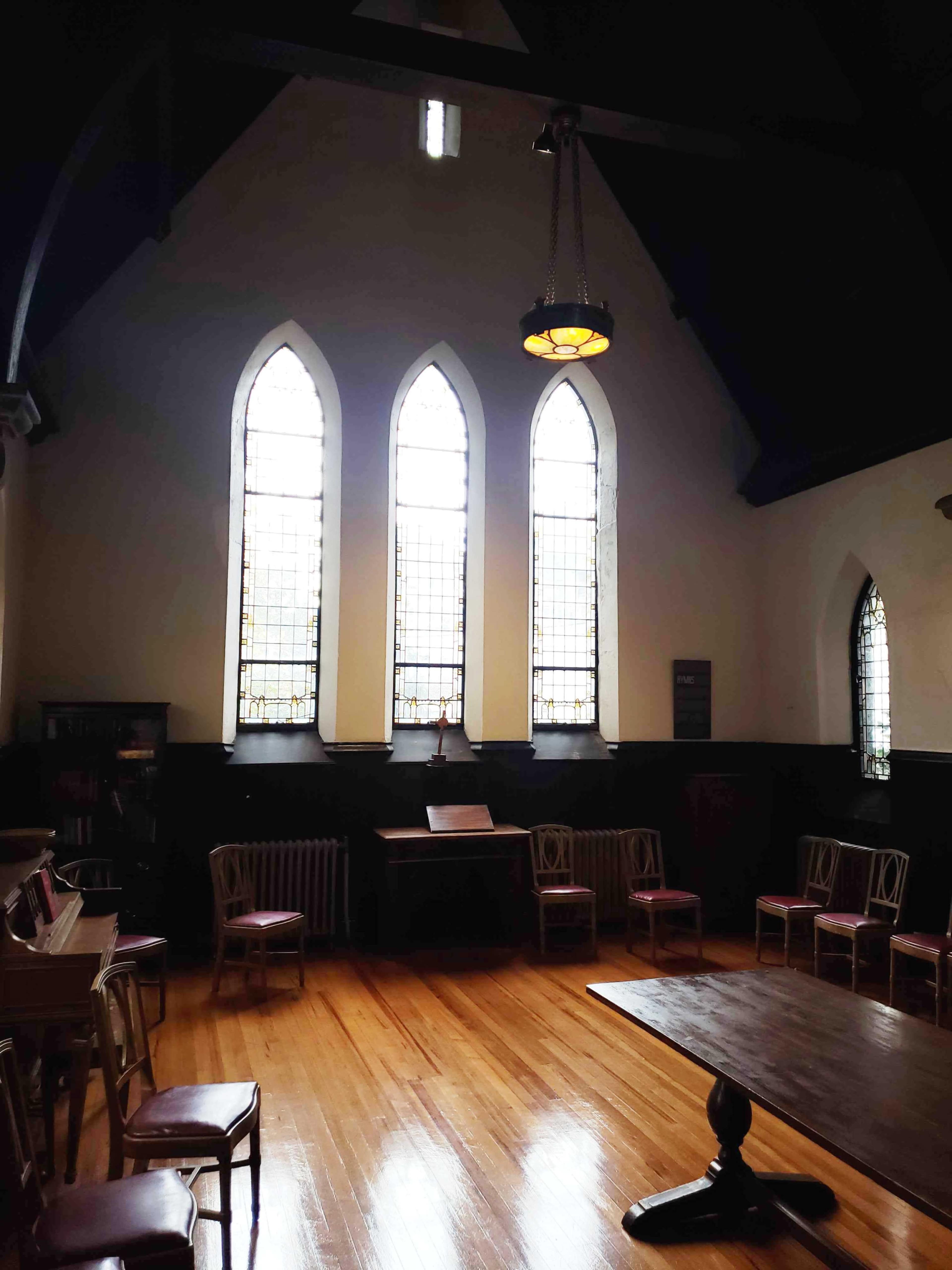 A spacious room with arched windows, a wooden table, and several chairs arranged around it.