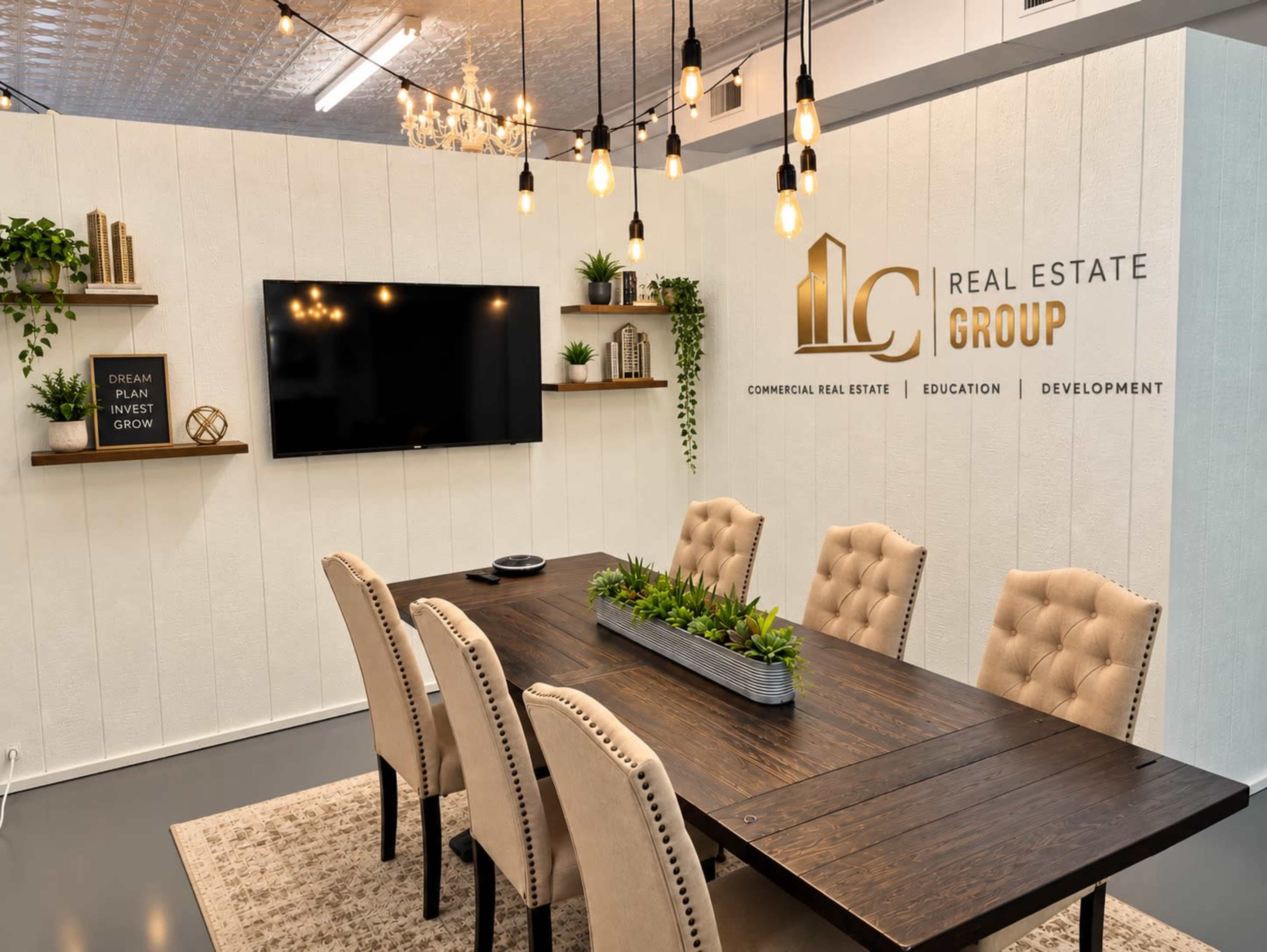 The image shows a modern conference room with a long wooden table surrounded by beige upholstered chairs, featuring a television screen and decorative plants on the walls.