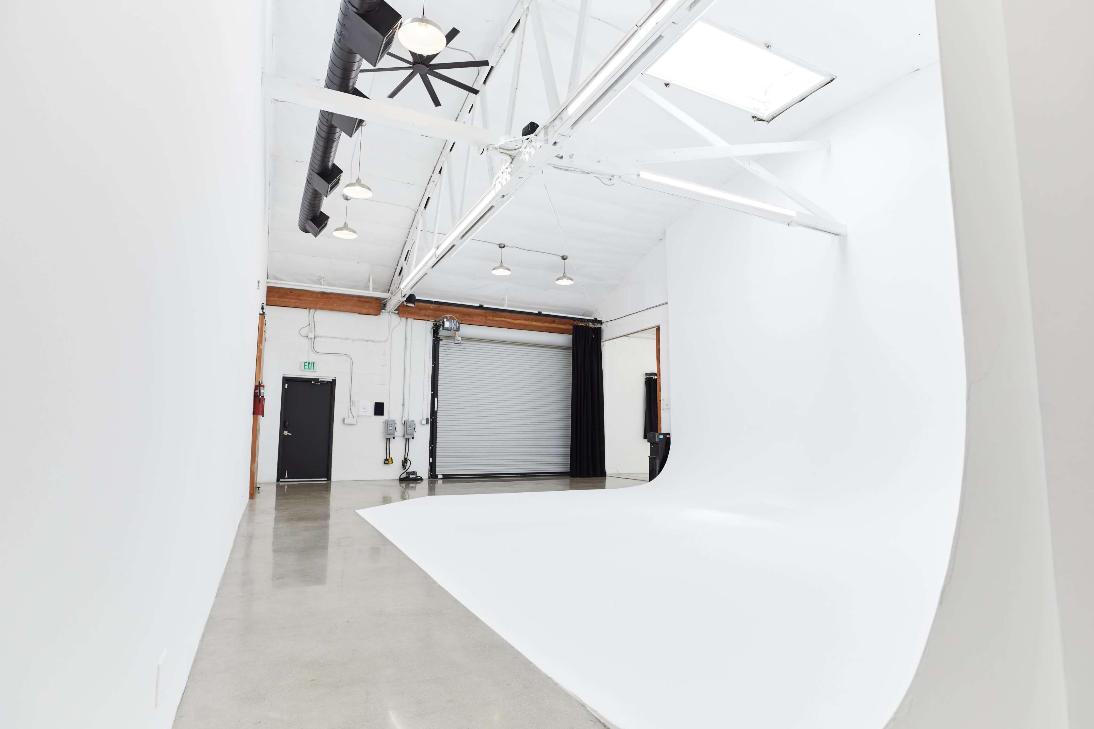The image shows a spacious photography studio featuring a large white backdrop, polished concrete flooring, and industrial lighting fixtures.