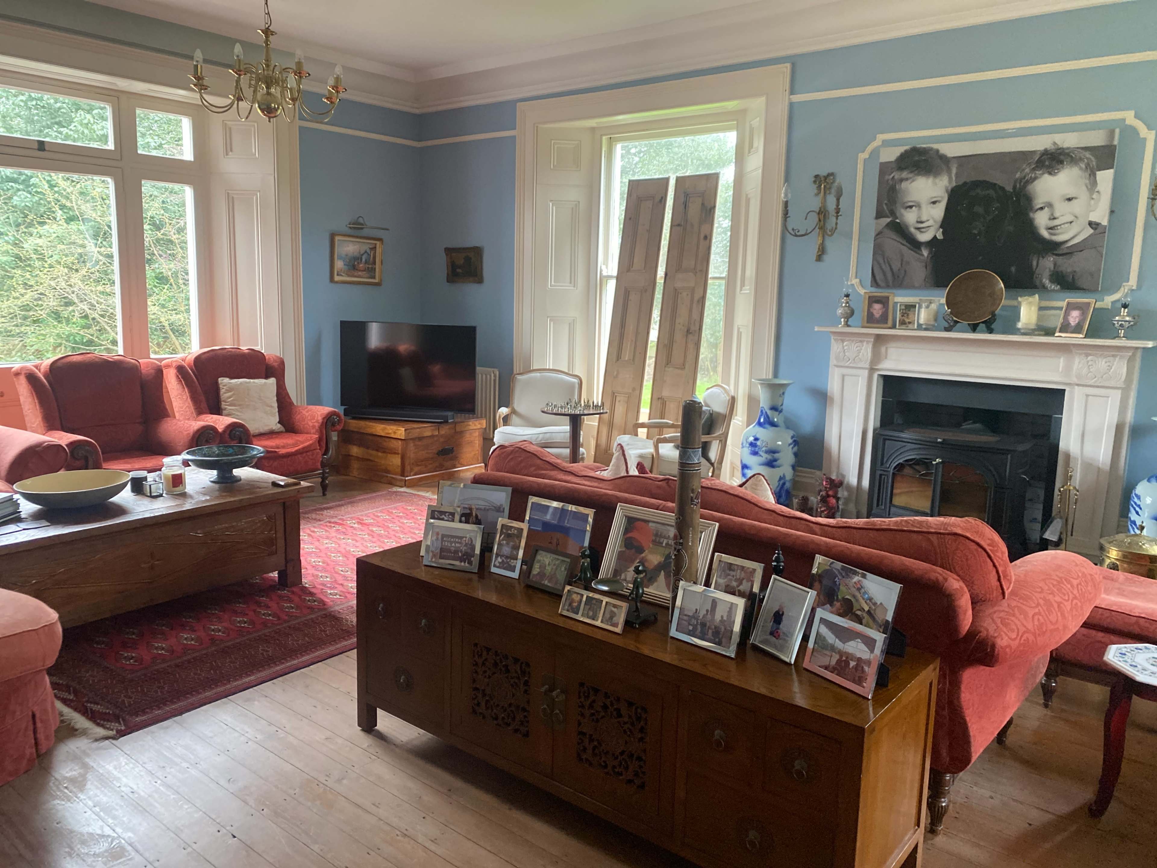 A cozy living room features two red sofas, a wooden coffee table, a television, and framed photographs displayed on a wooden sideboard.