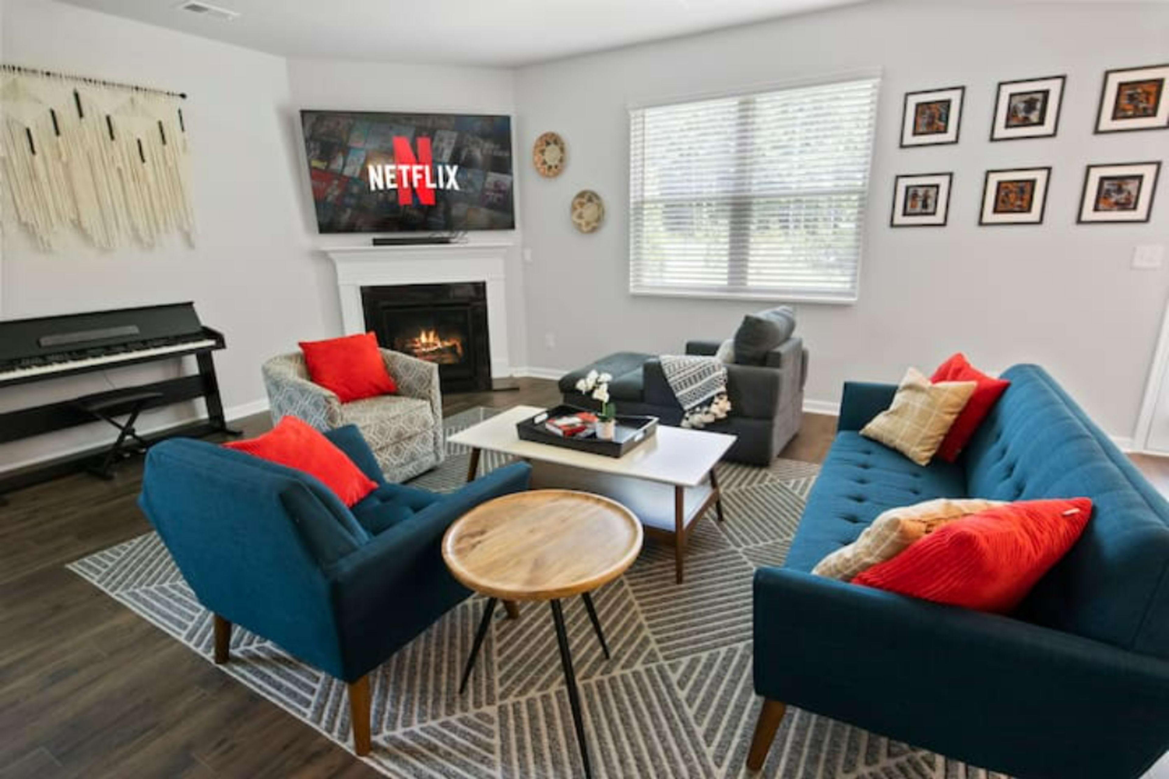 The living room features a fireplace, a large TV displaying the Netflix logo, and blue sofas arranged around a coffee table with decorative accents.