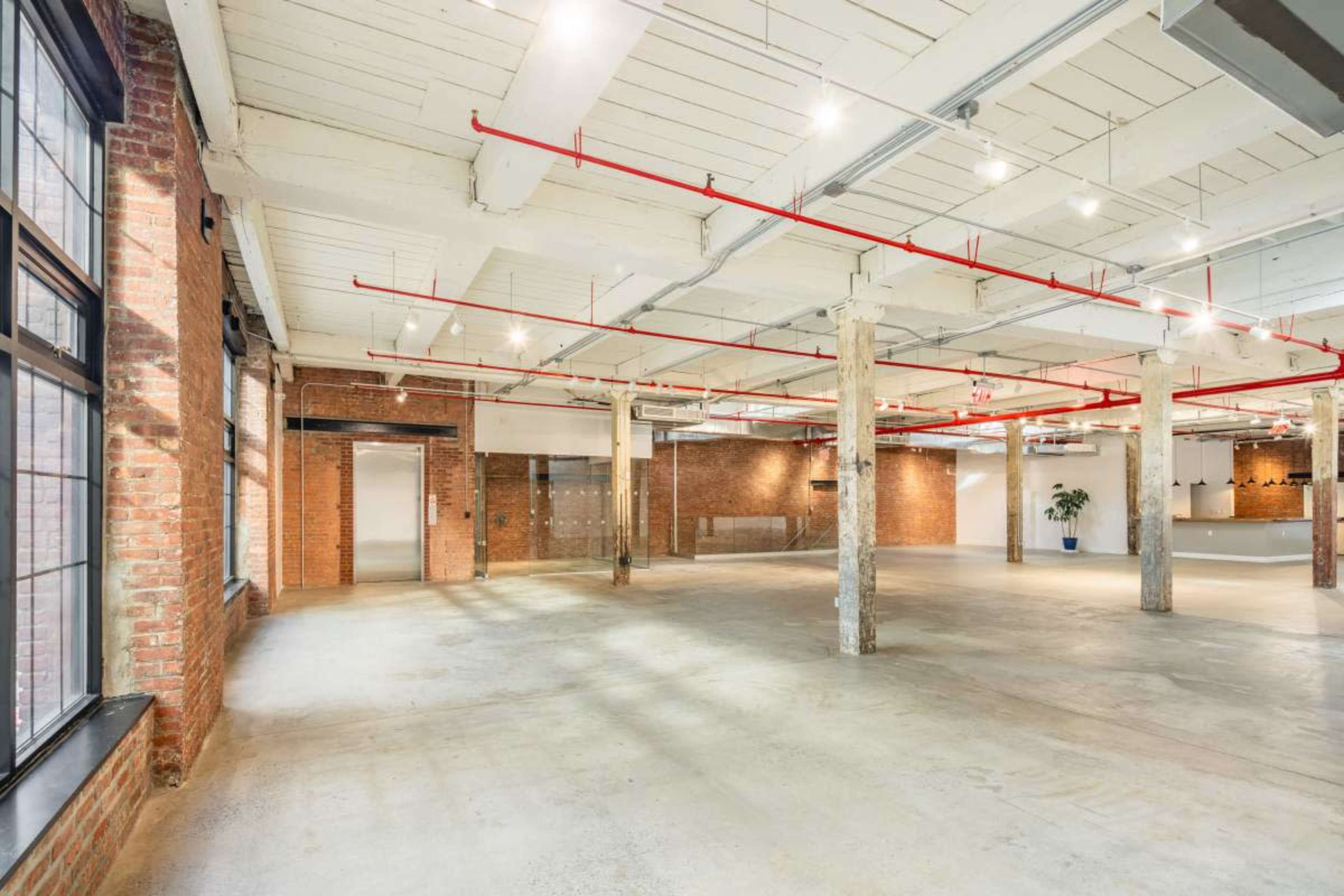 The image shows a spacious industrial-style interior with exposed brick walls, concrete flooring, and overhead lighting.