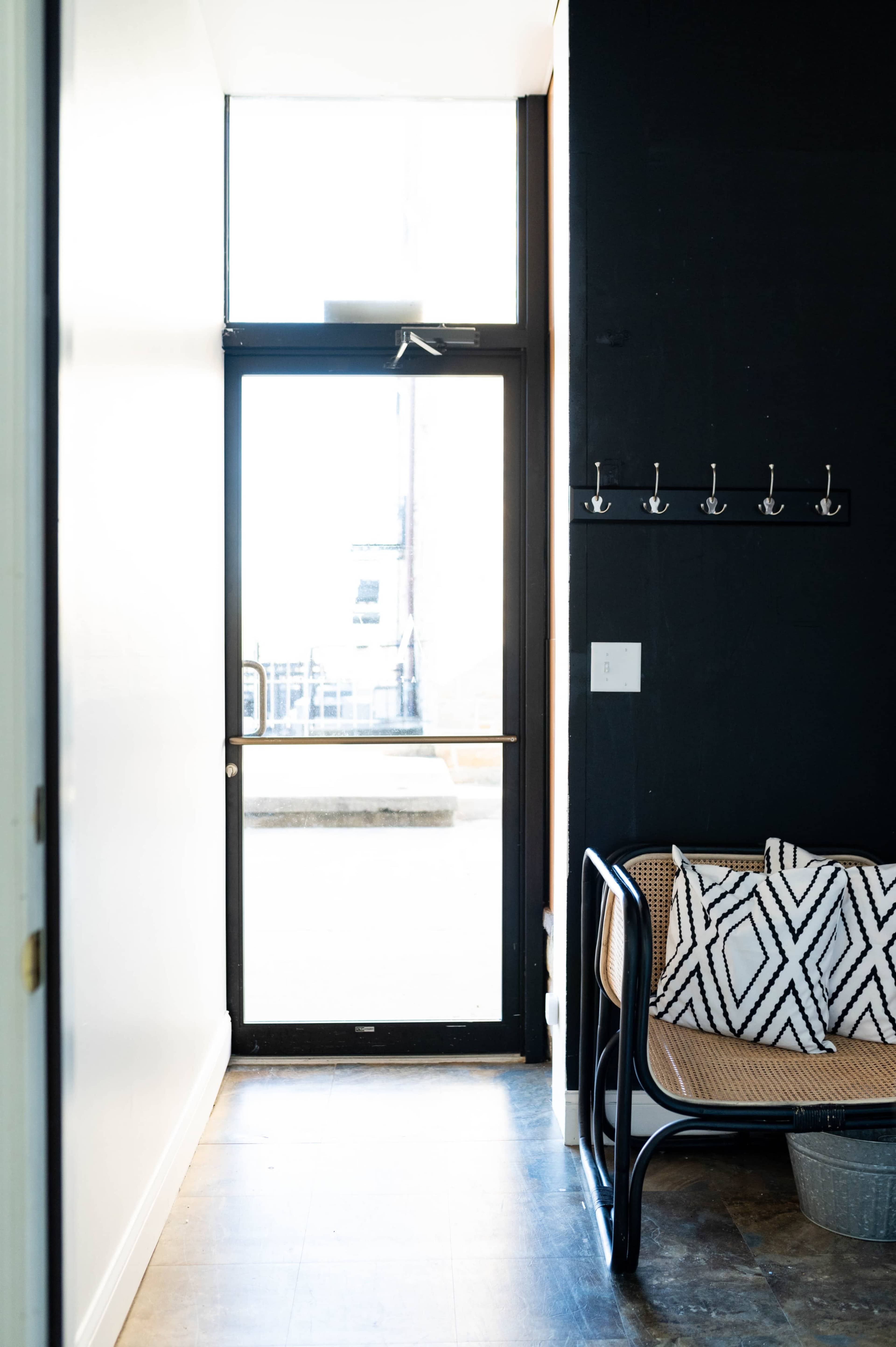A hallway features a glass door leading to an outdoor area, with a bench and hooks on the wall.