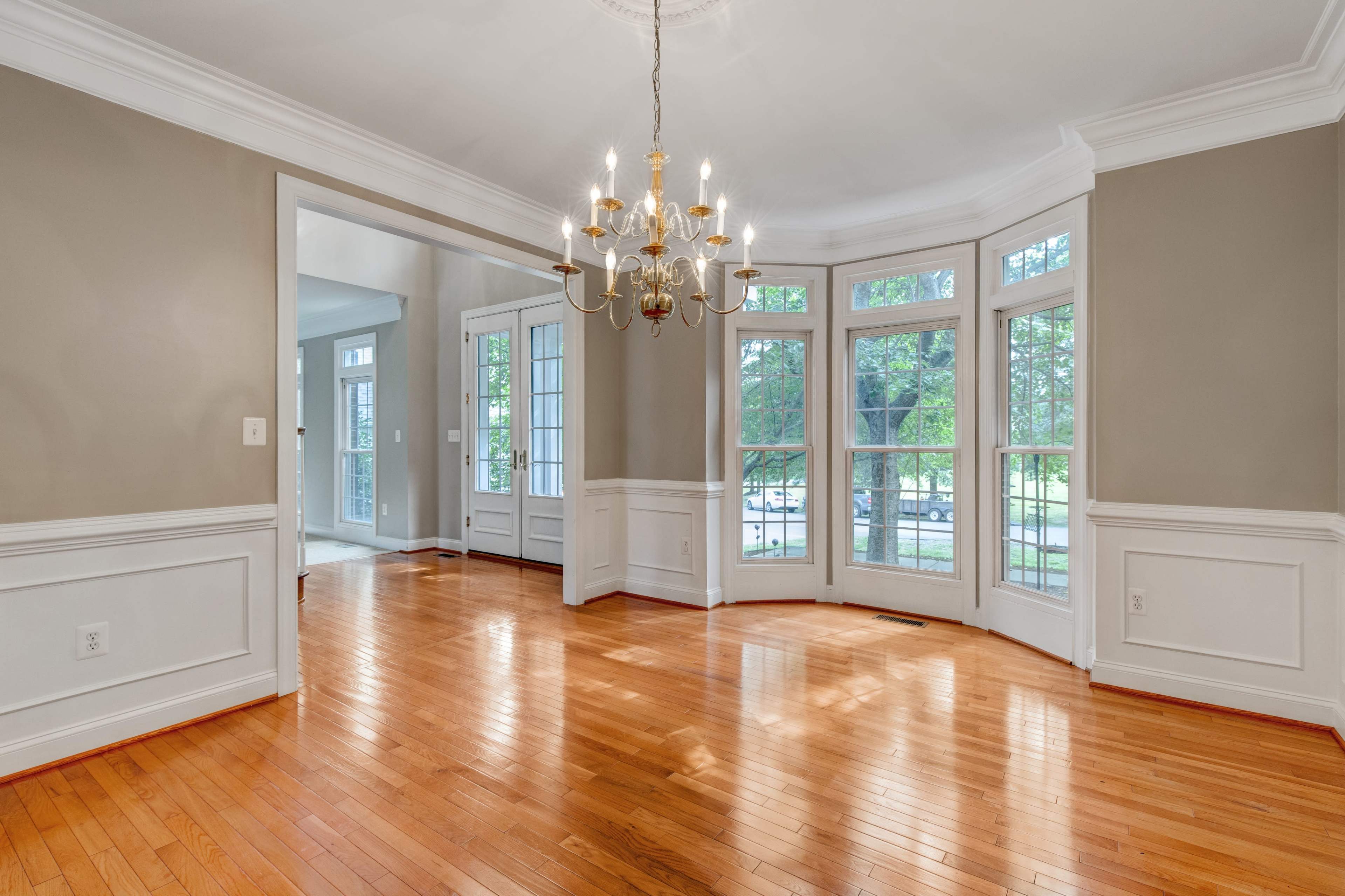 The room features hardwood flooring, large windows, and a chandelier illuminating the space.