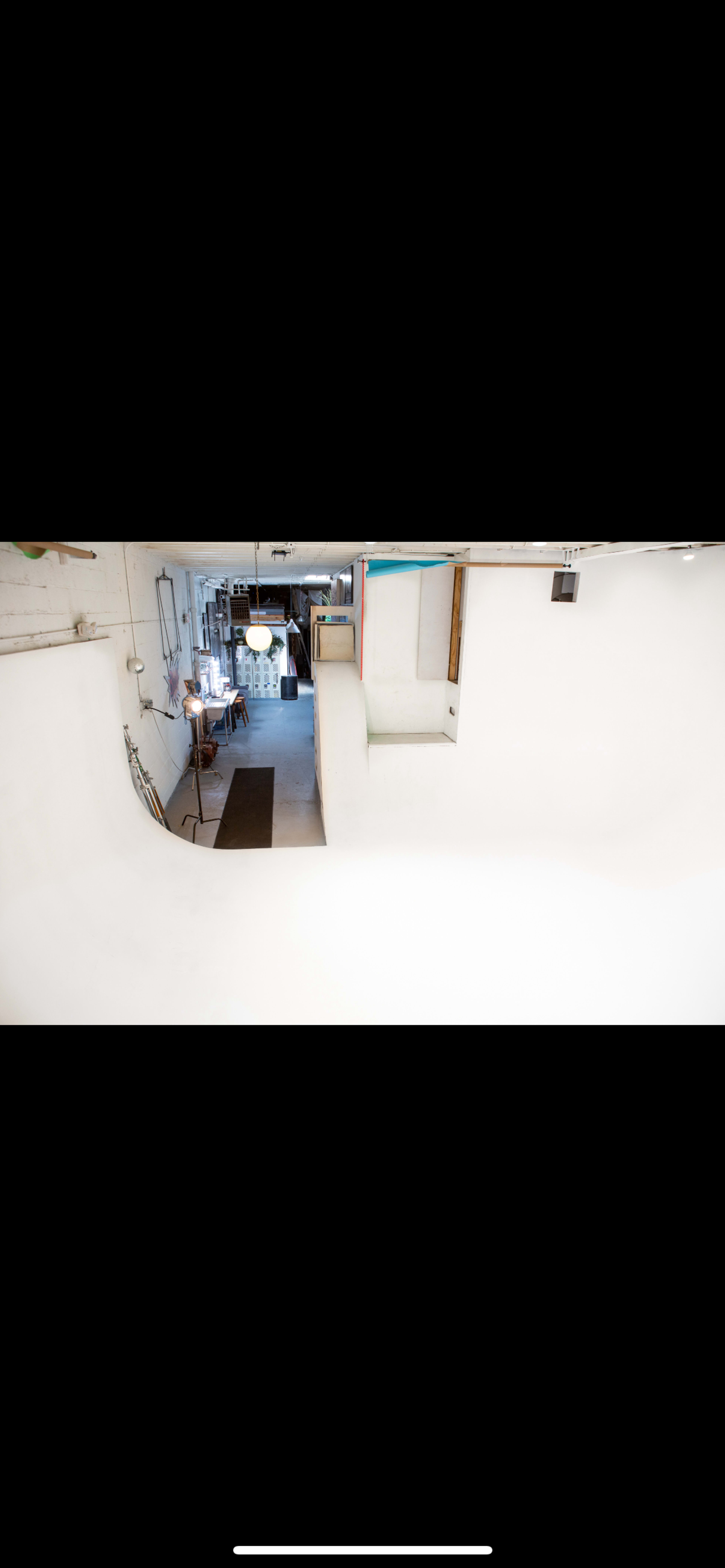 The image shows a spacious interior with a curved white wall, leading to a well-lit area containing furniture and equipment.