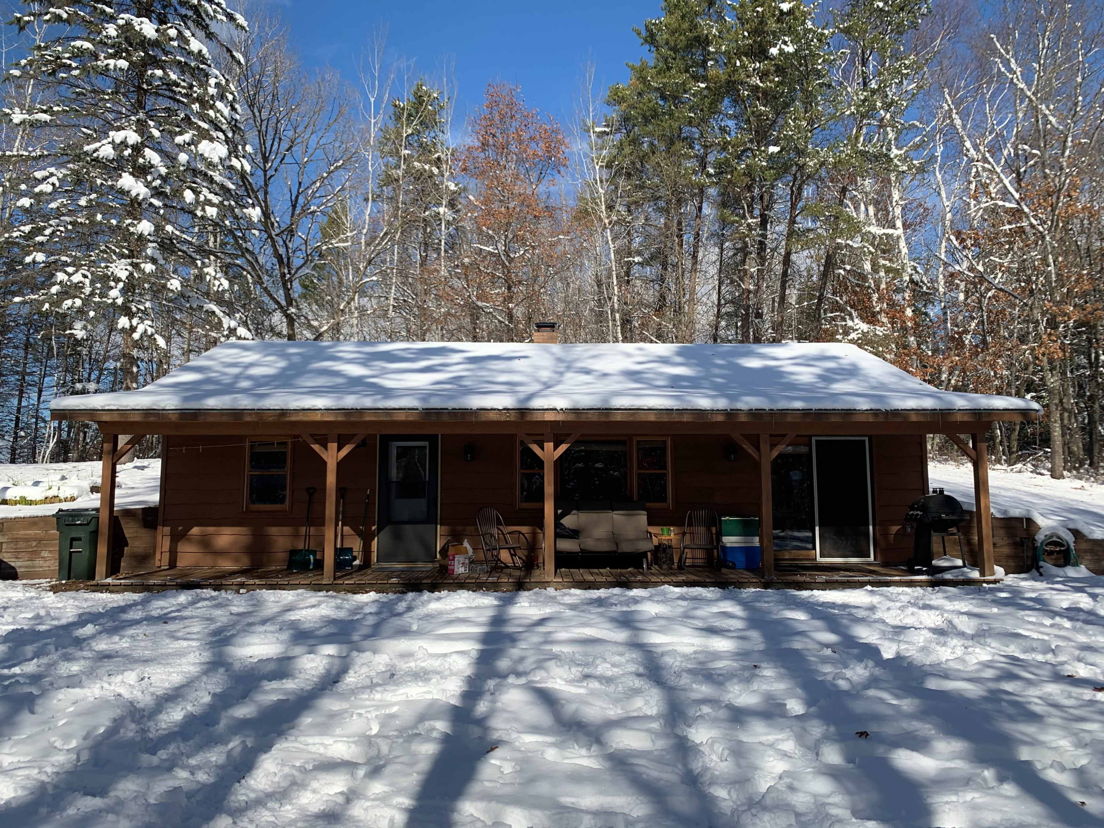 A wooden cabin with a snow-covered roof is surrounded by trees in a winter landscape.