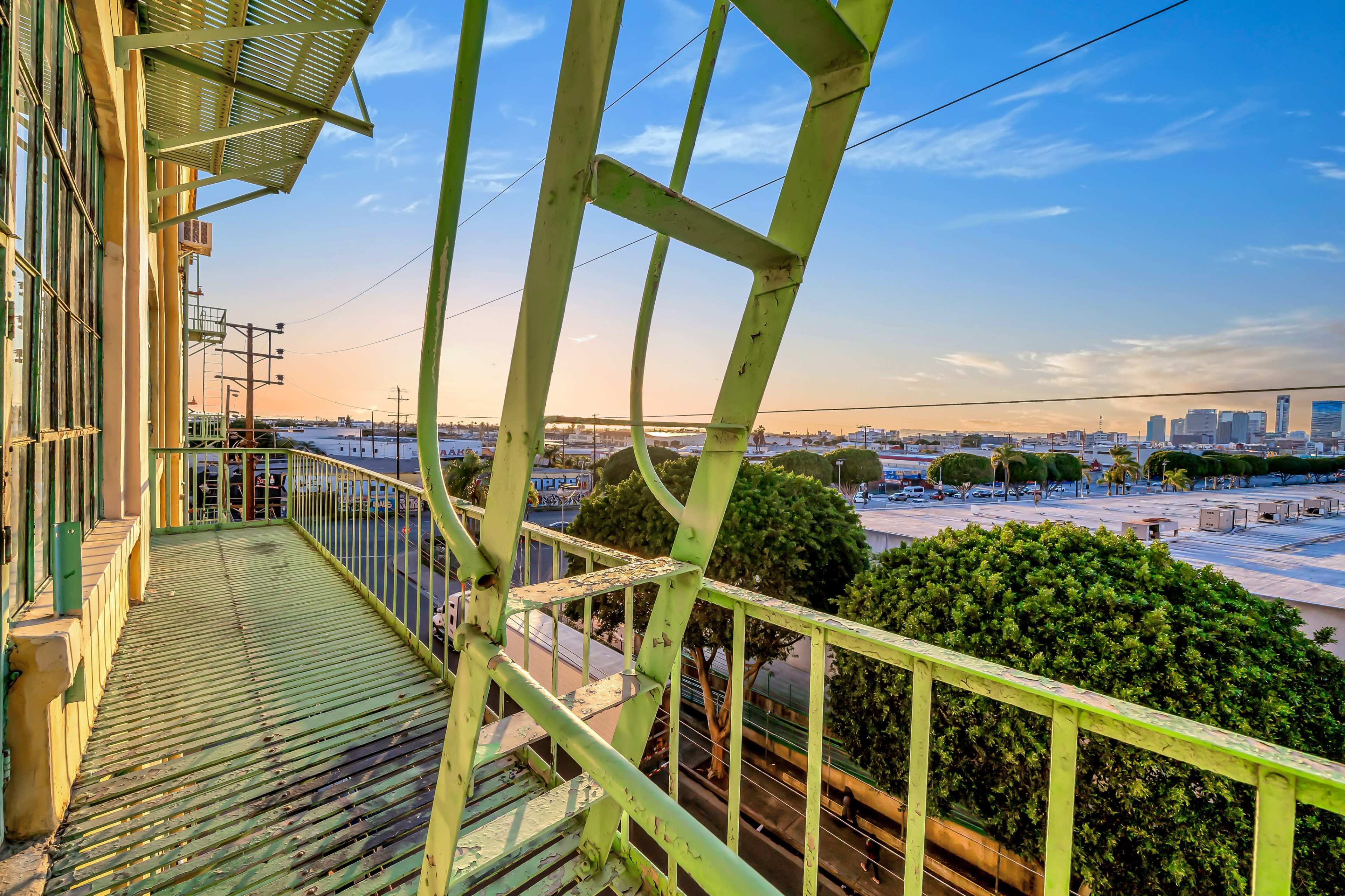 A green metal fire escape extending from a building, overlooking a parking lot and skyline under a clear blue sky.