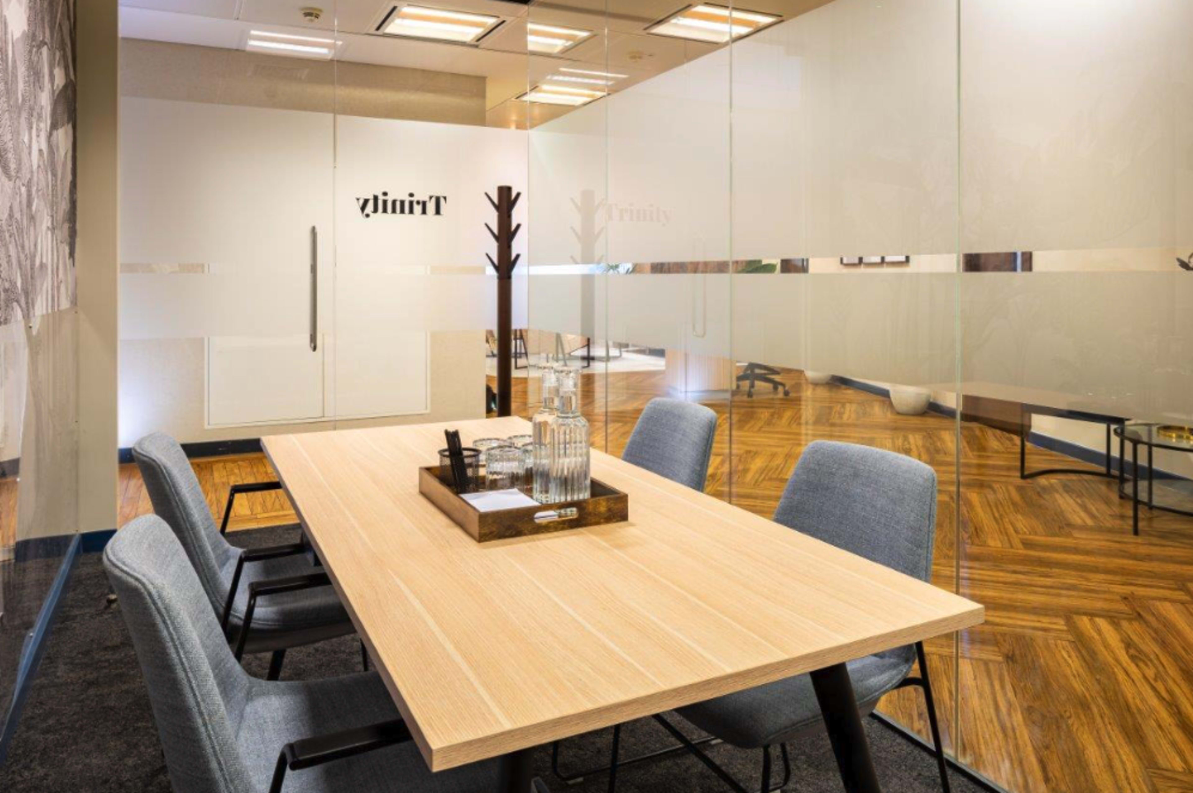 A modern conference room features a wooden table surrounded by gray chairs, with glass walls and a minimalist decor.