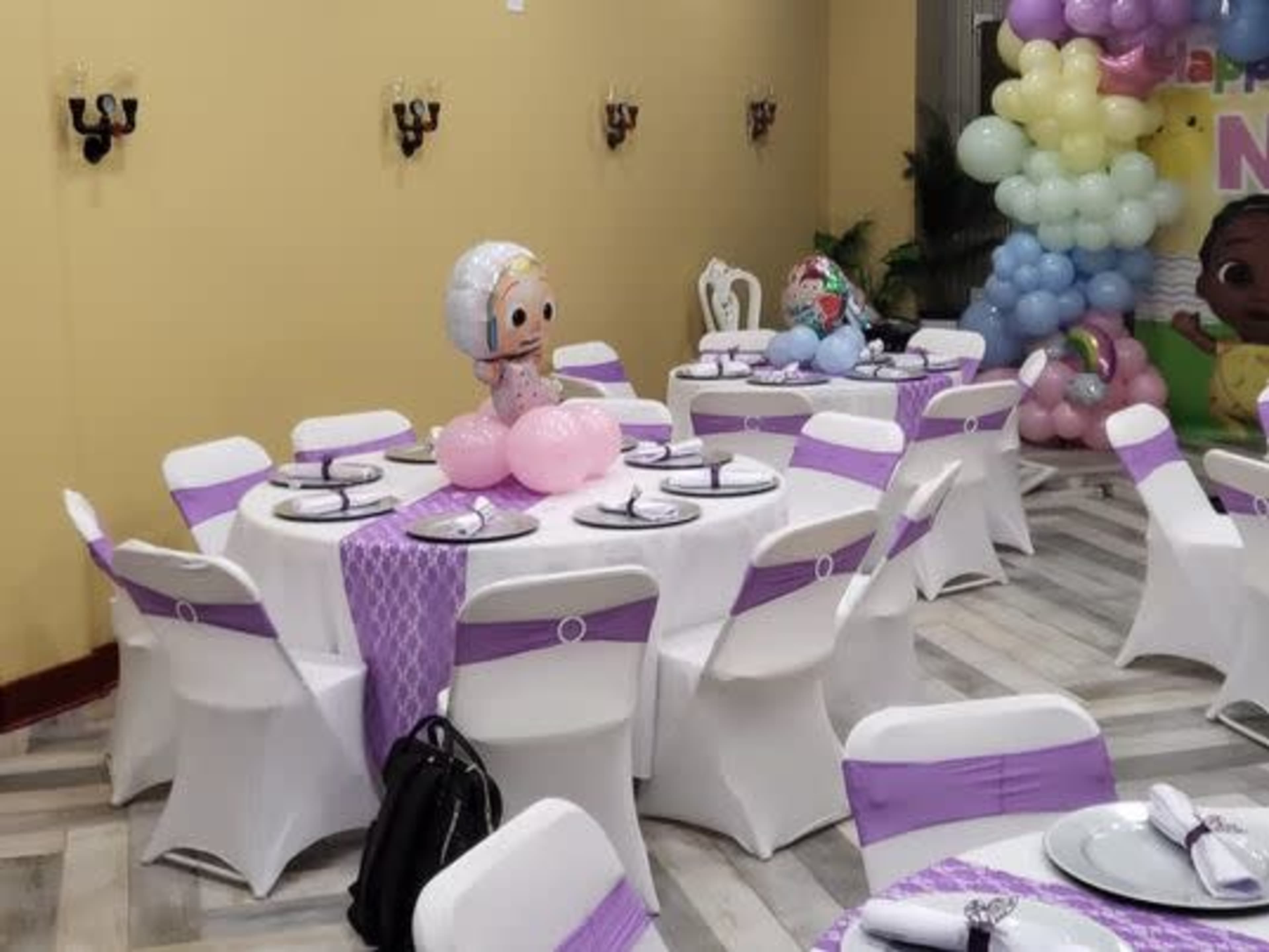 A party room with tables set in white and purple, decorated with balloons and character figures.