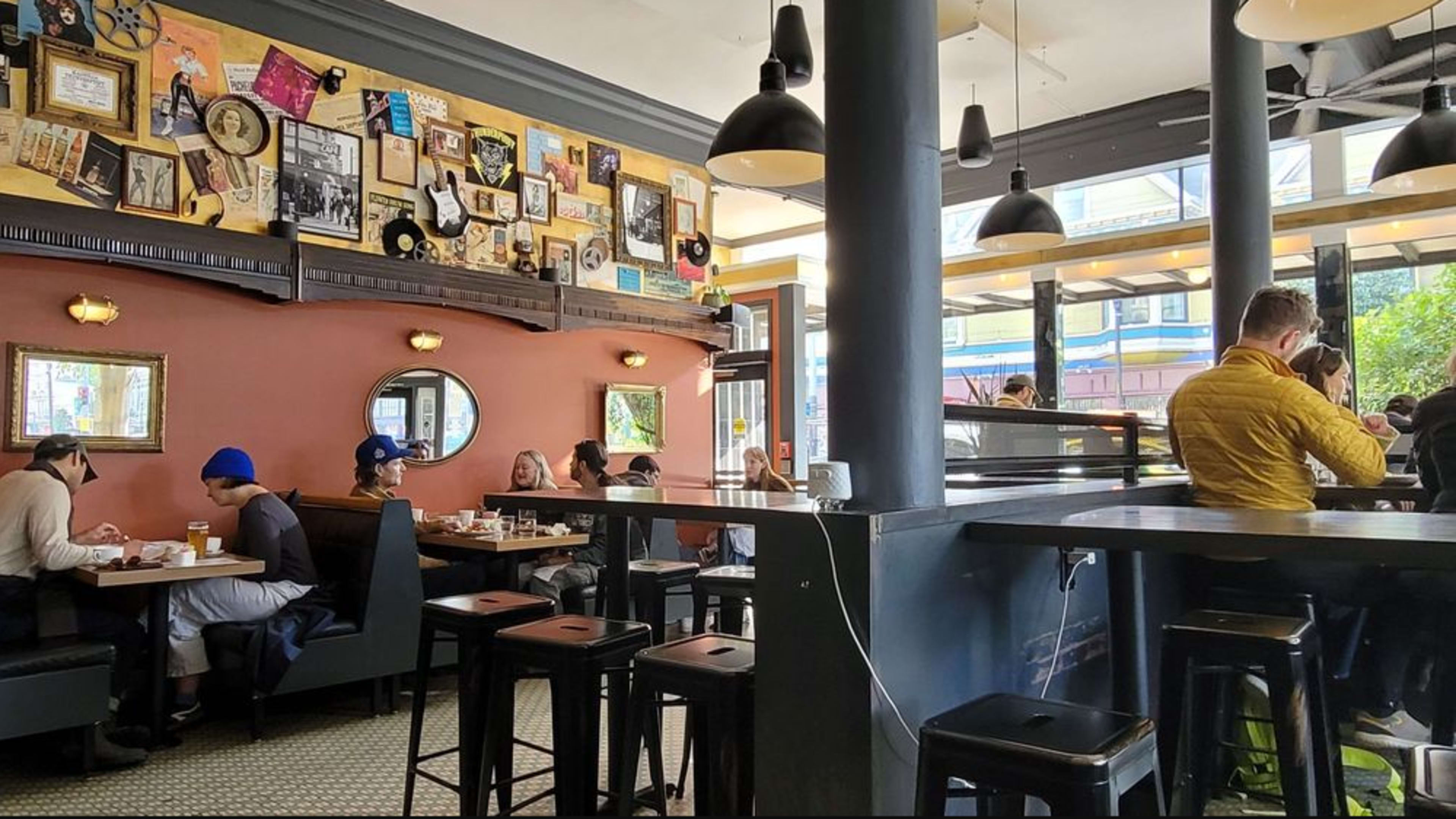 The image shows a bustling café with a mix of patrons seated at tables and a bar, featuring decorated walls adorned with vintage memorabilia.