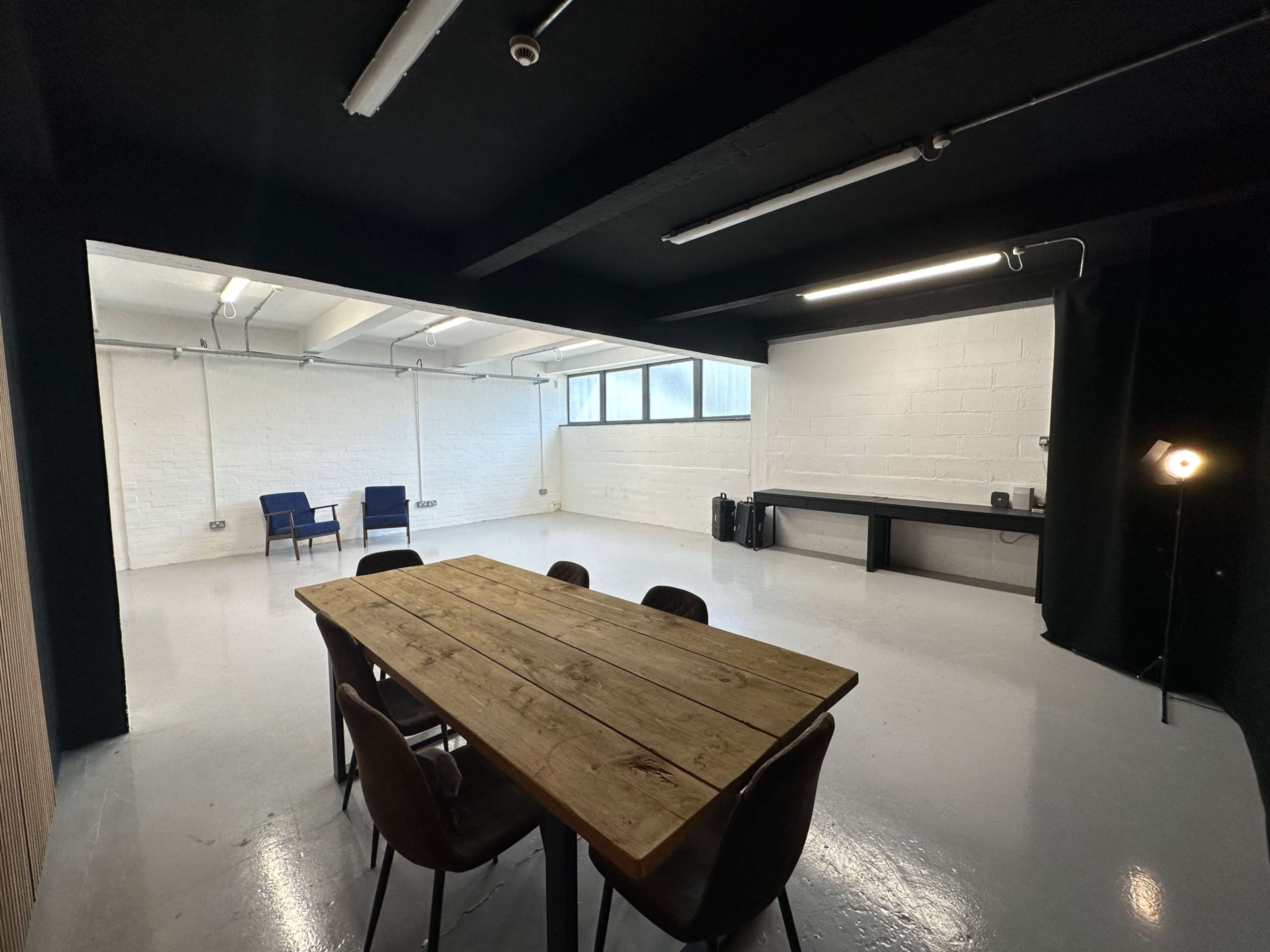 A minimalist meeting room with a wooden table, black chairs, and two blue chairs in a well-lit, white-walled space.