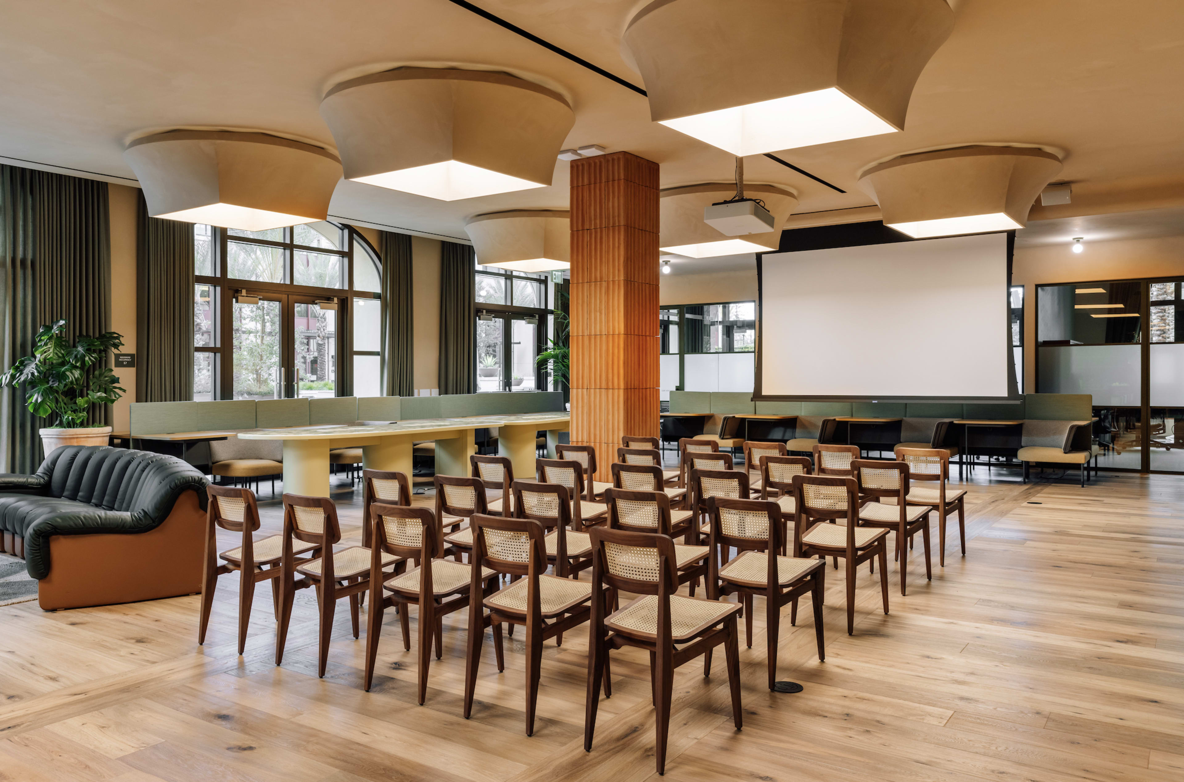 A spacious conference room with rows of wooden chairs, a large table, and a projector screen at one end.