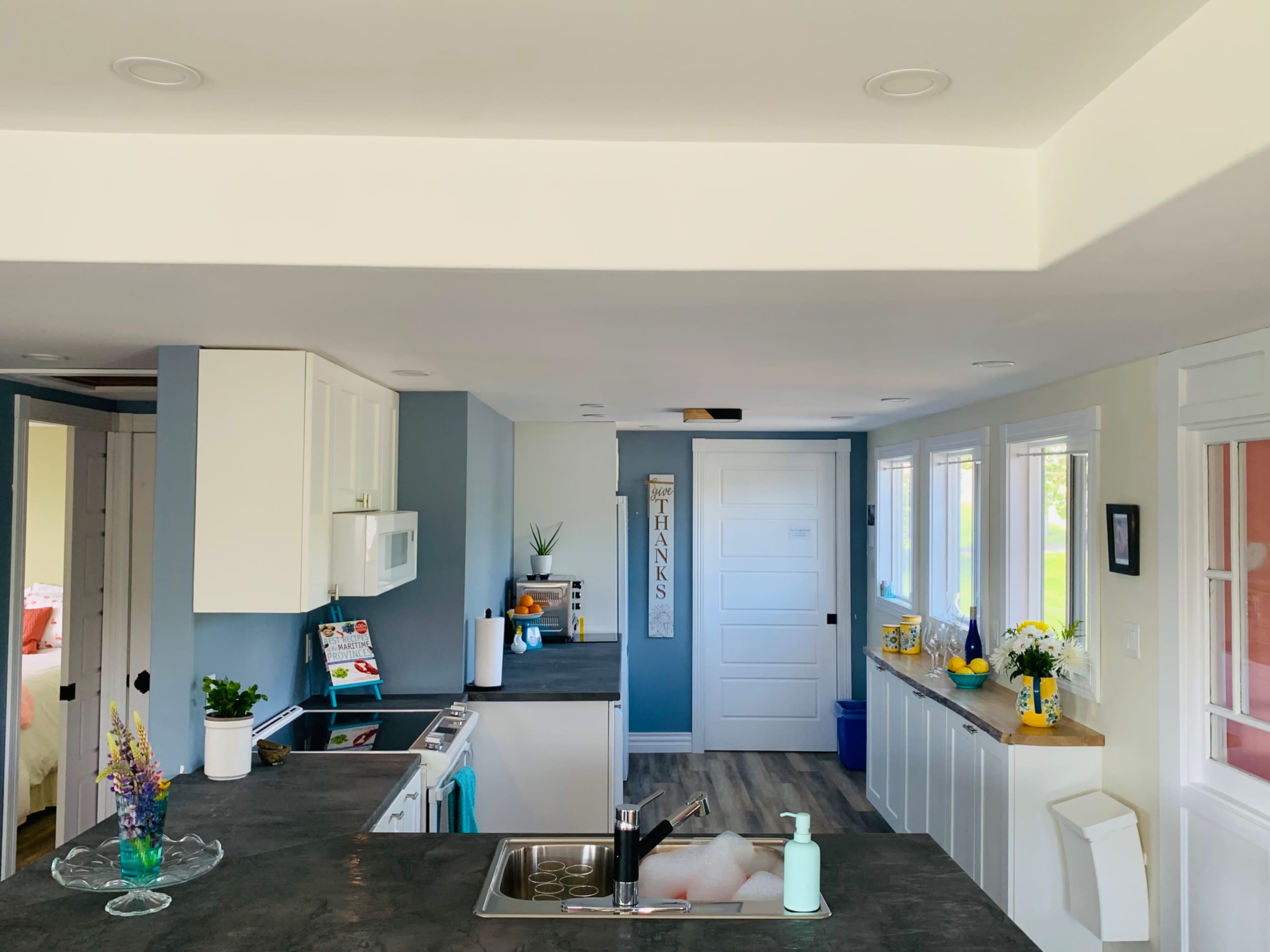A modern kitchen with a gray countertop, white cabinetry, and a view of a nearby door and window area.