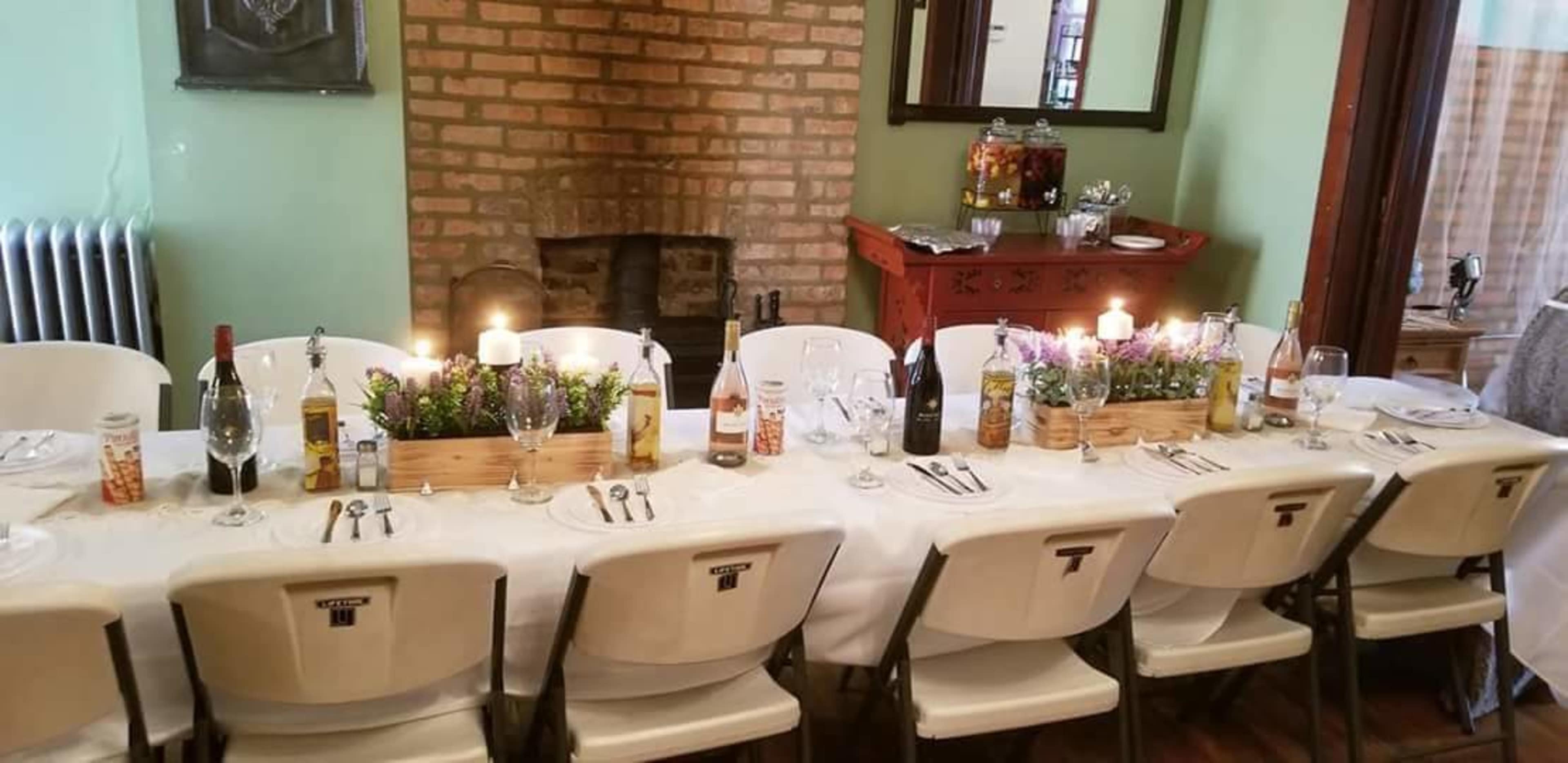 A long table is set for a meal with plates, glasses, and candles, arranged neatly in a room featuring a brick wall and a decorative sideboard.